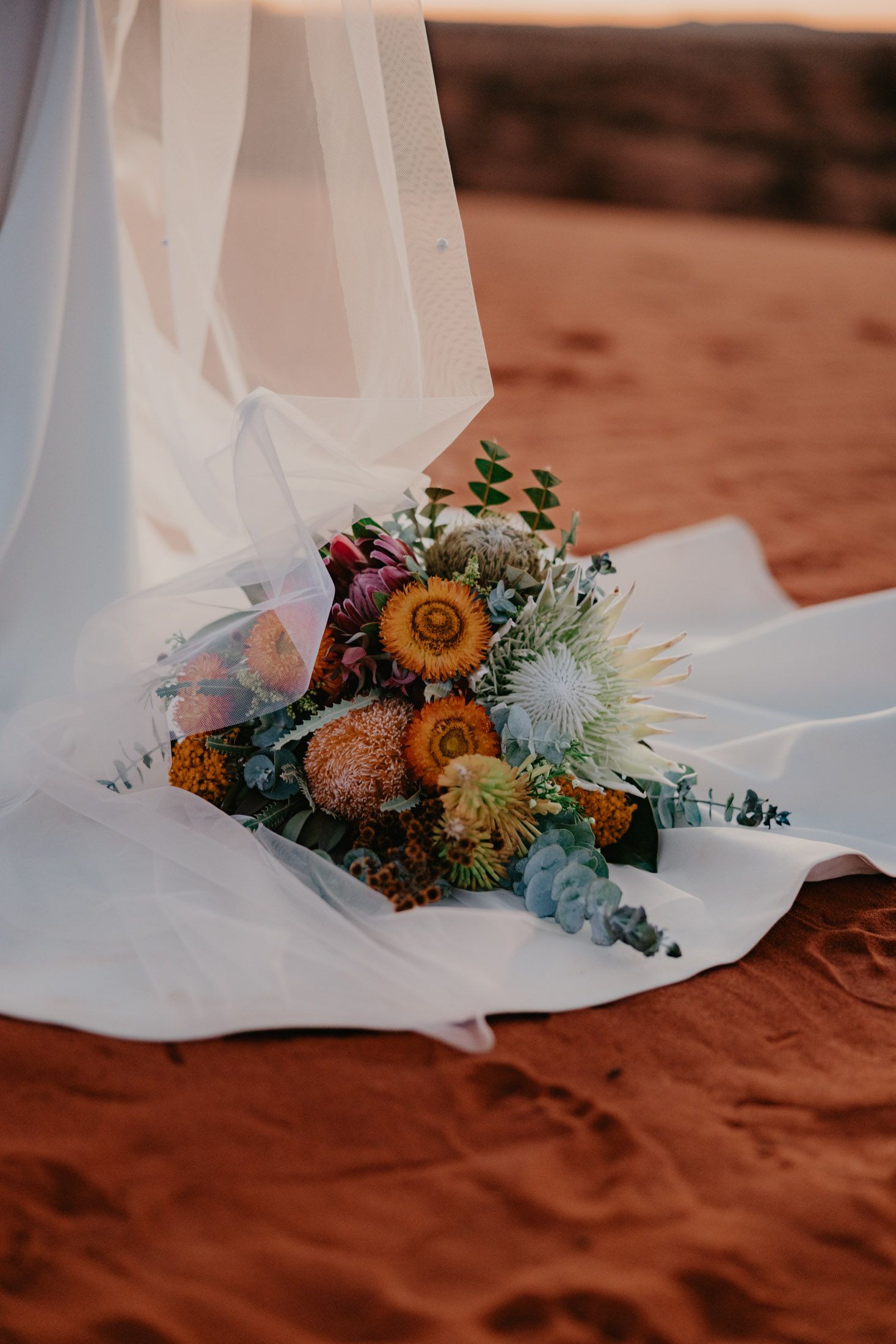 Brides native floral bouquet placed on wedding dress train and veil on red pindan dunes near Exmouth, Wa