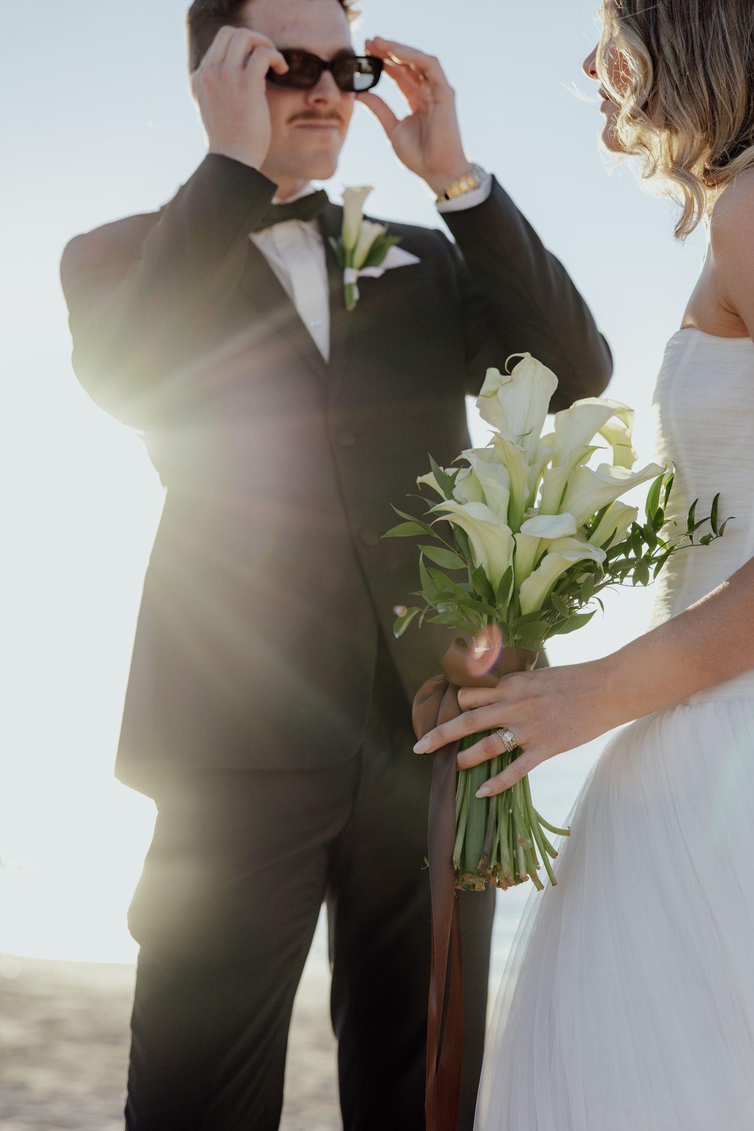 Groom adjusts sunglasses with Bride holding flowers looking at him during wedding portrait session, Ningaloo Reef, Exmouth, WA