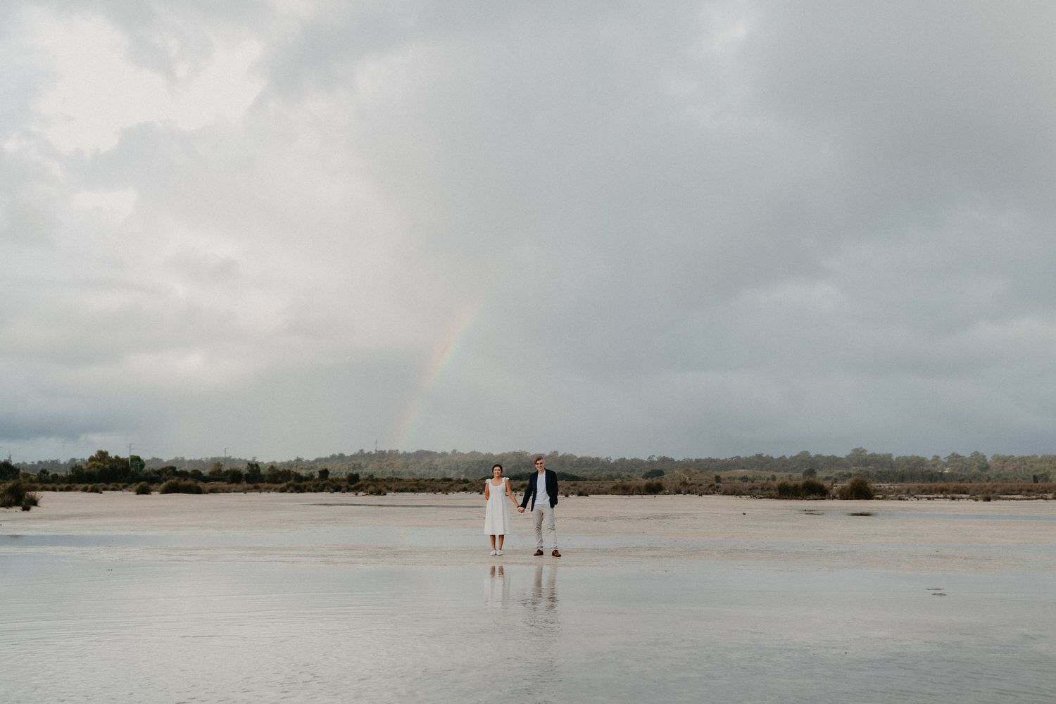 Couple holding hands at their engagement session with a rainbow in the background