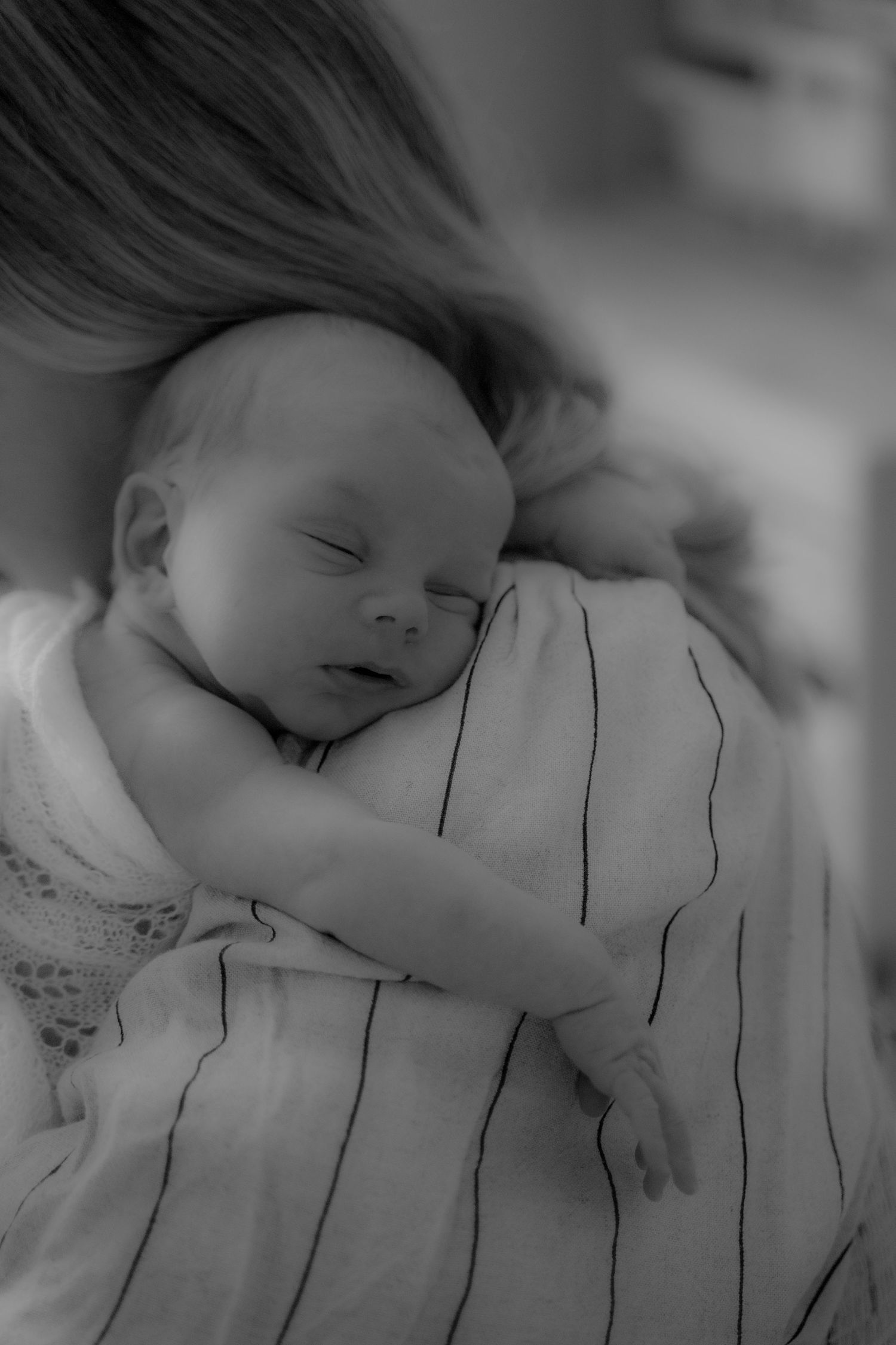 A sleeping baby rests peacefully on white and black striped bedding in a black and white photograph.