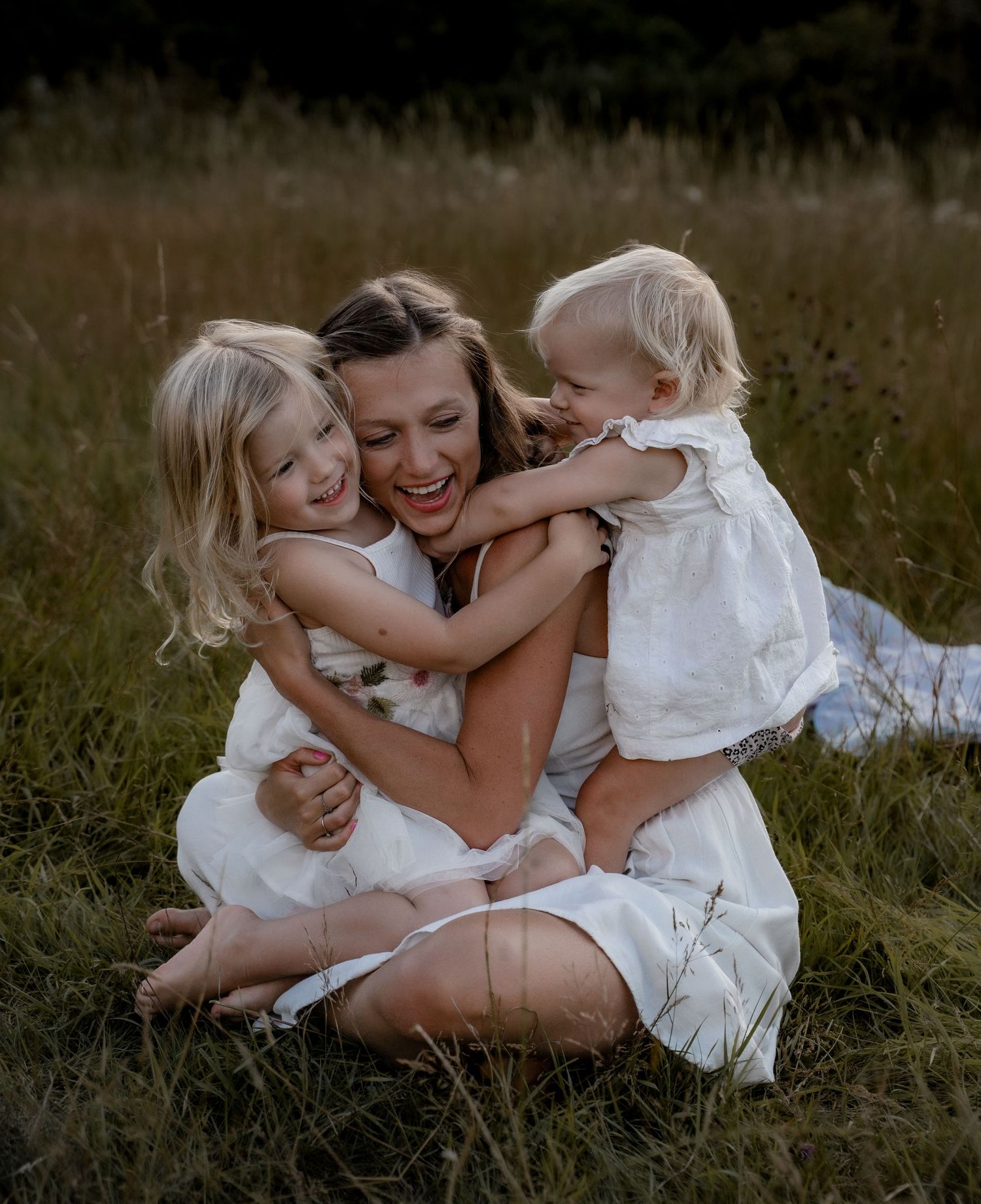 mum cuddling her 2 daughters outsdoors in the golden light in white clothes