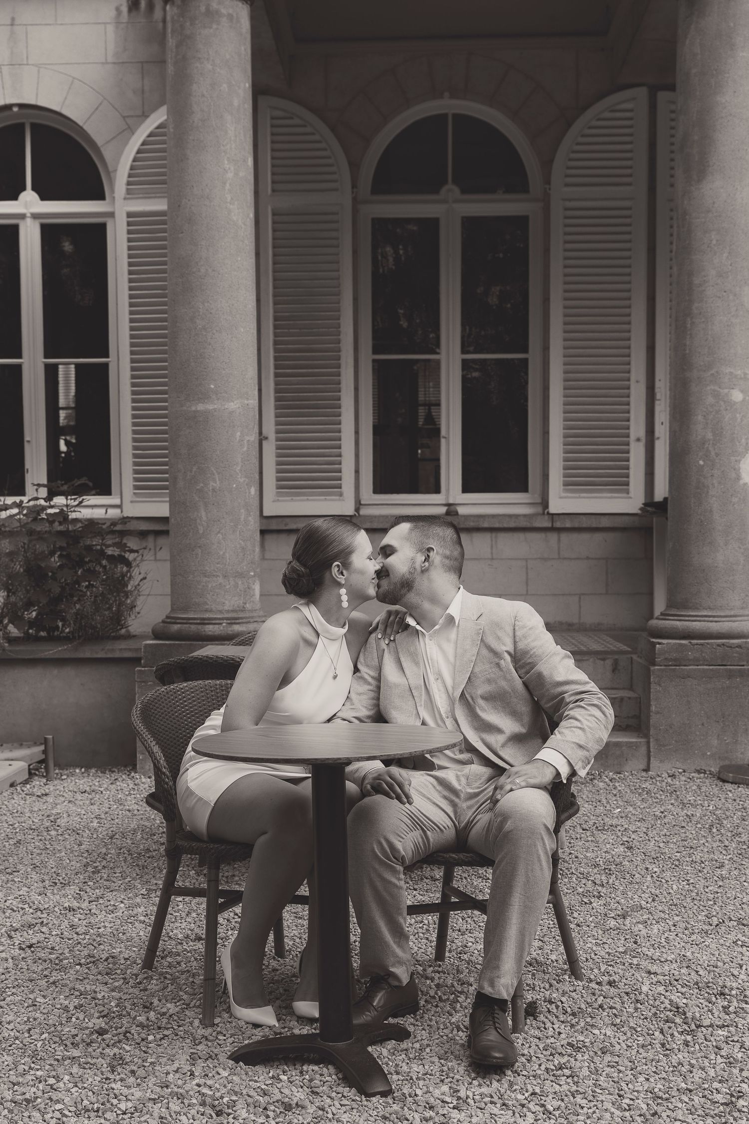 Couple shares intimate moment on bench in courtyard with classic architecture.