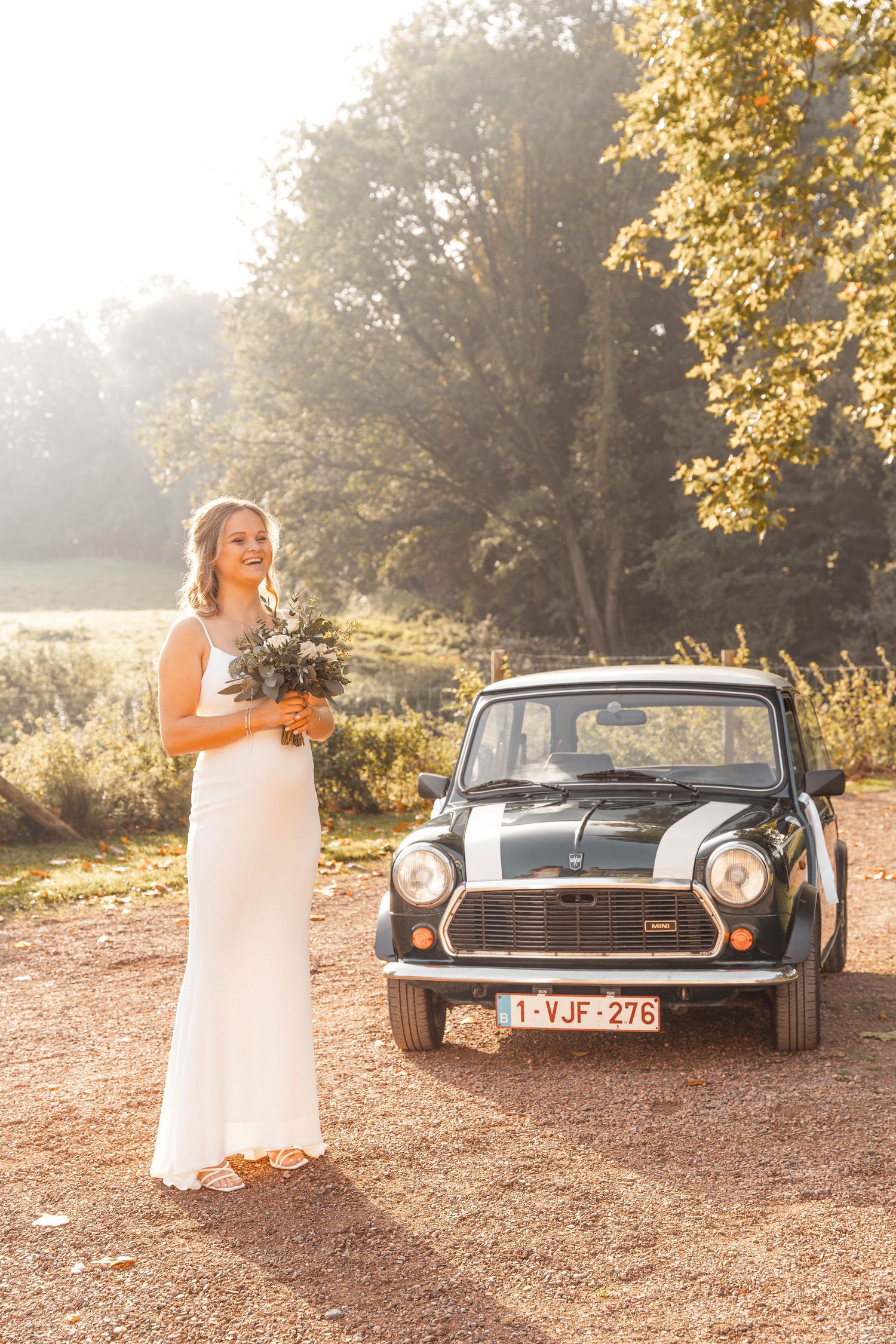 Classic Mini Cooper parked on dirt road with autumn trees and golden sunlight.