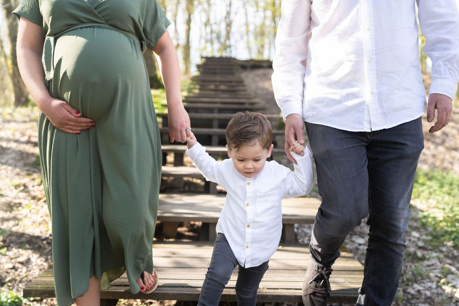 A couple walks with their small child on wooden steps in a wooded area.