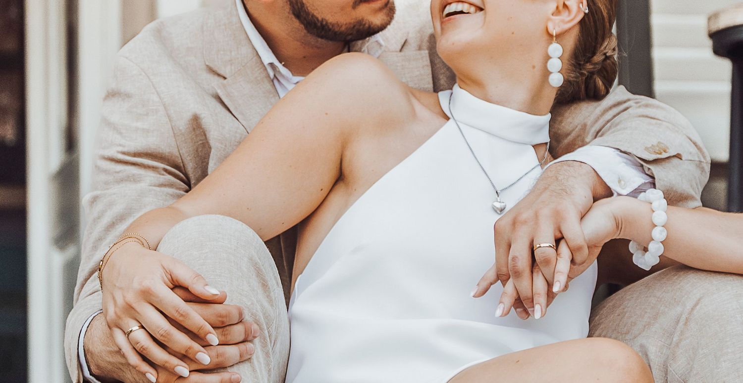 A couple shares a tender moment while sitting together, with the bride in a white halter dress.
