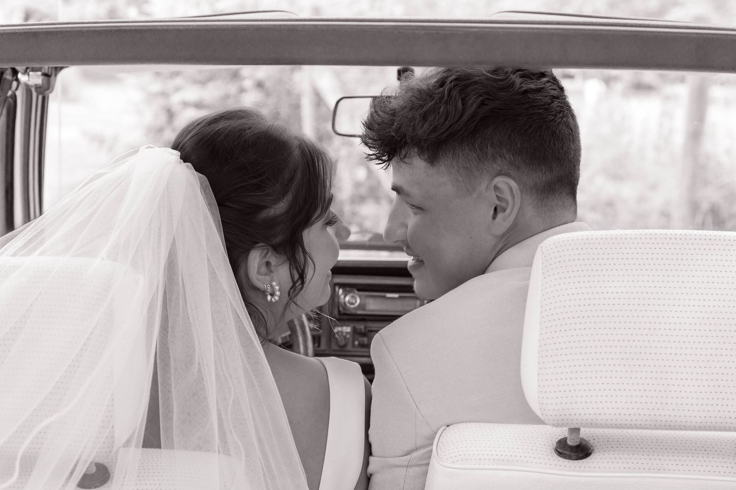Black and white photo capturing a tender moment inside a vintage car.