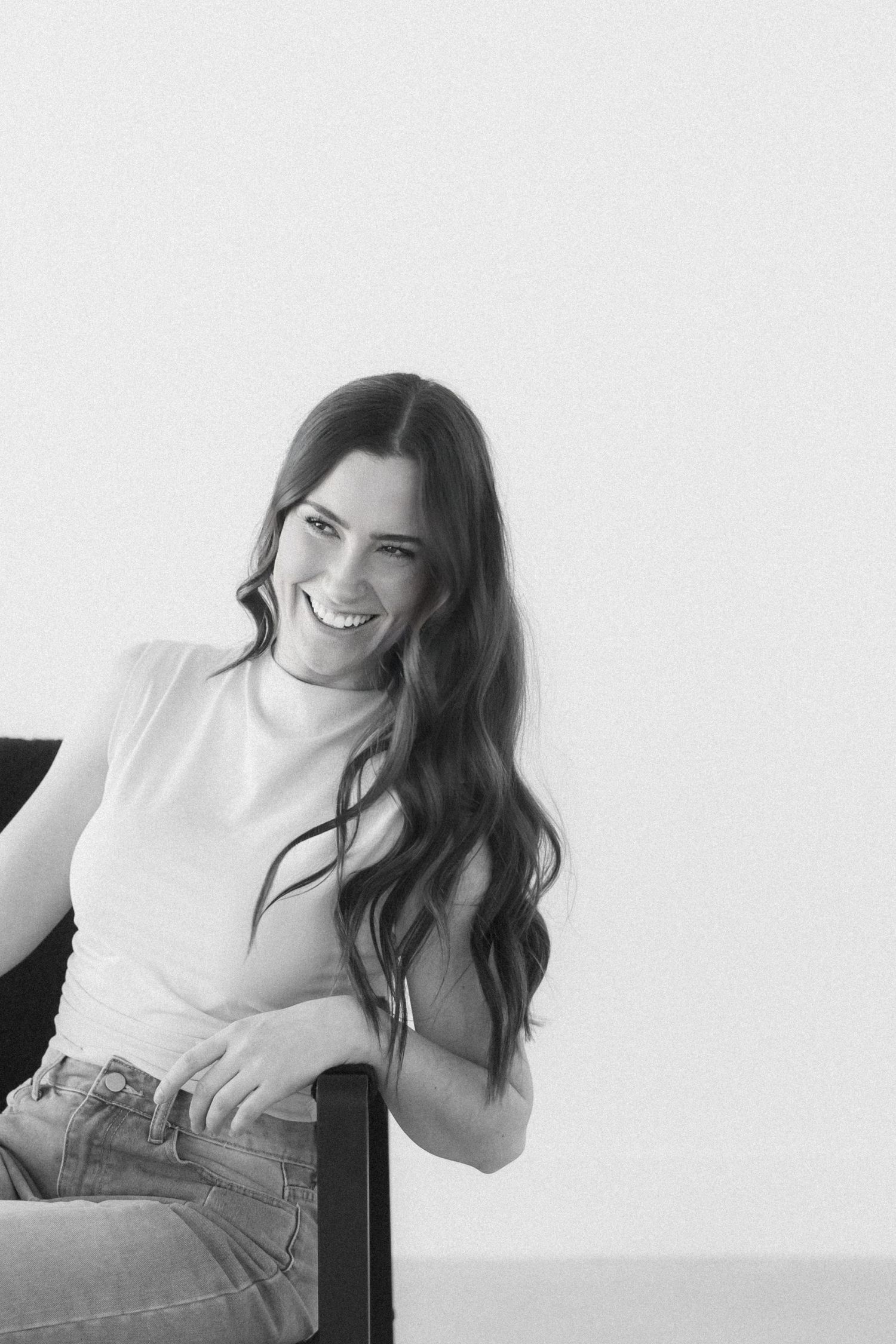 A series of black and white portraits showing a person in a white top and jeans sitting and smiling against a light background.