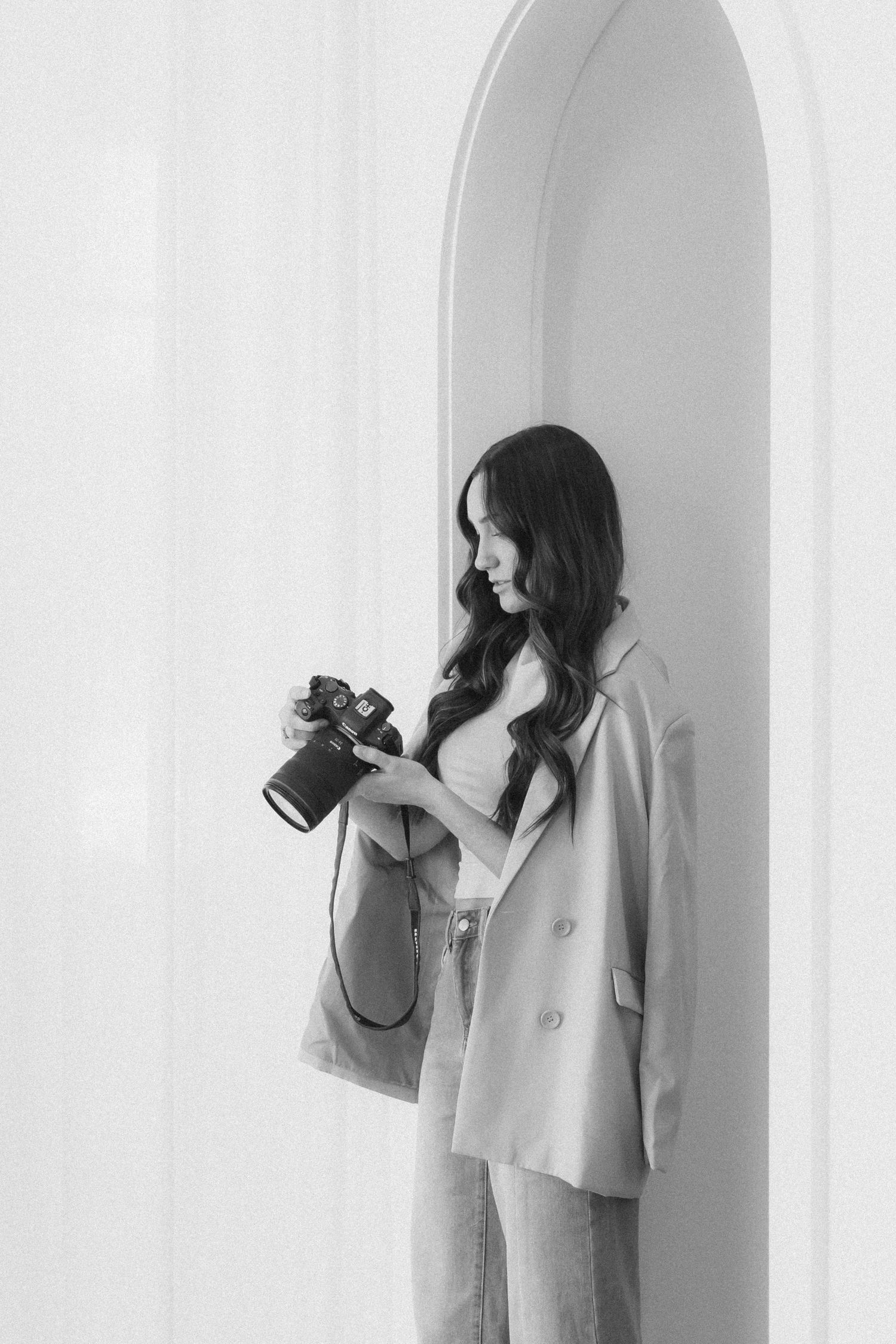 A series of minimalist black and white photos showing a person in a light coat holding a camera against a white wall.