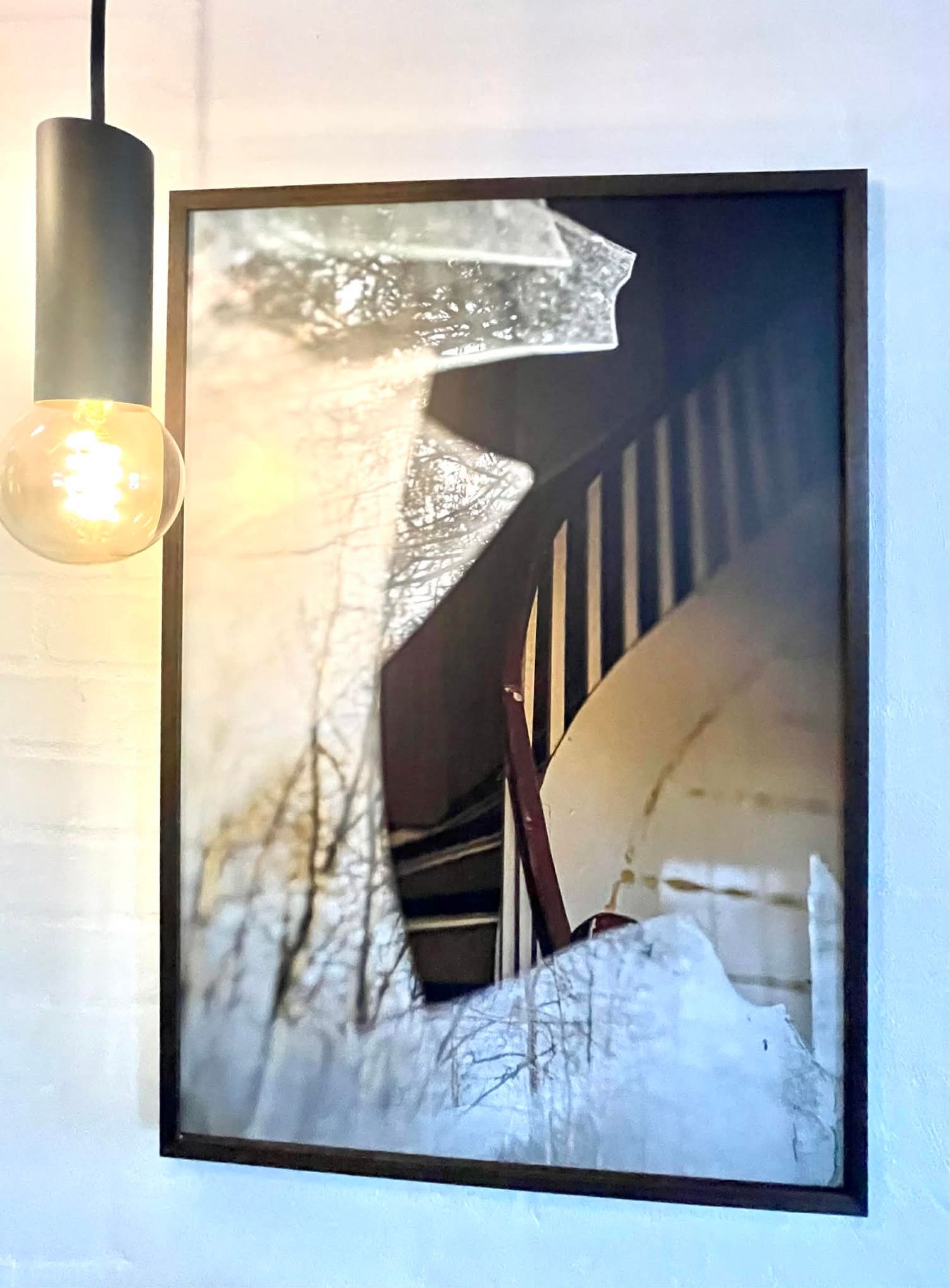 Fotokunst af en gammel, snoet trappe bag et knust vindue. I glassets refleksion ses træer