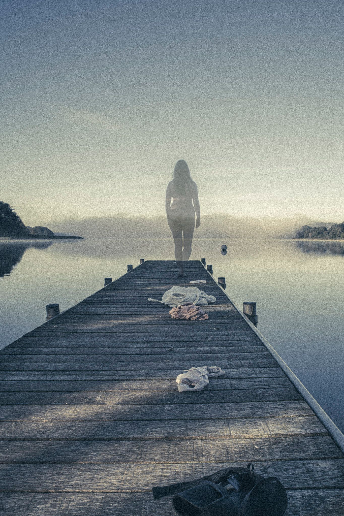 Fotografi af Margit Givskov af en nøgen kvinde der står for enden af en badebro og er blevet gennemsigtig.