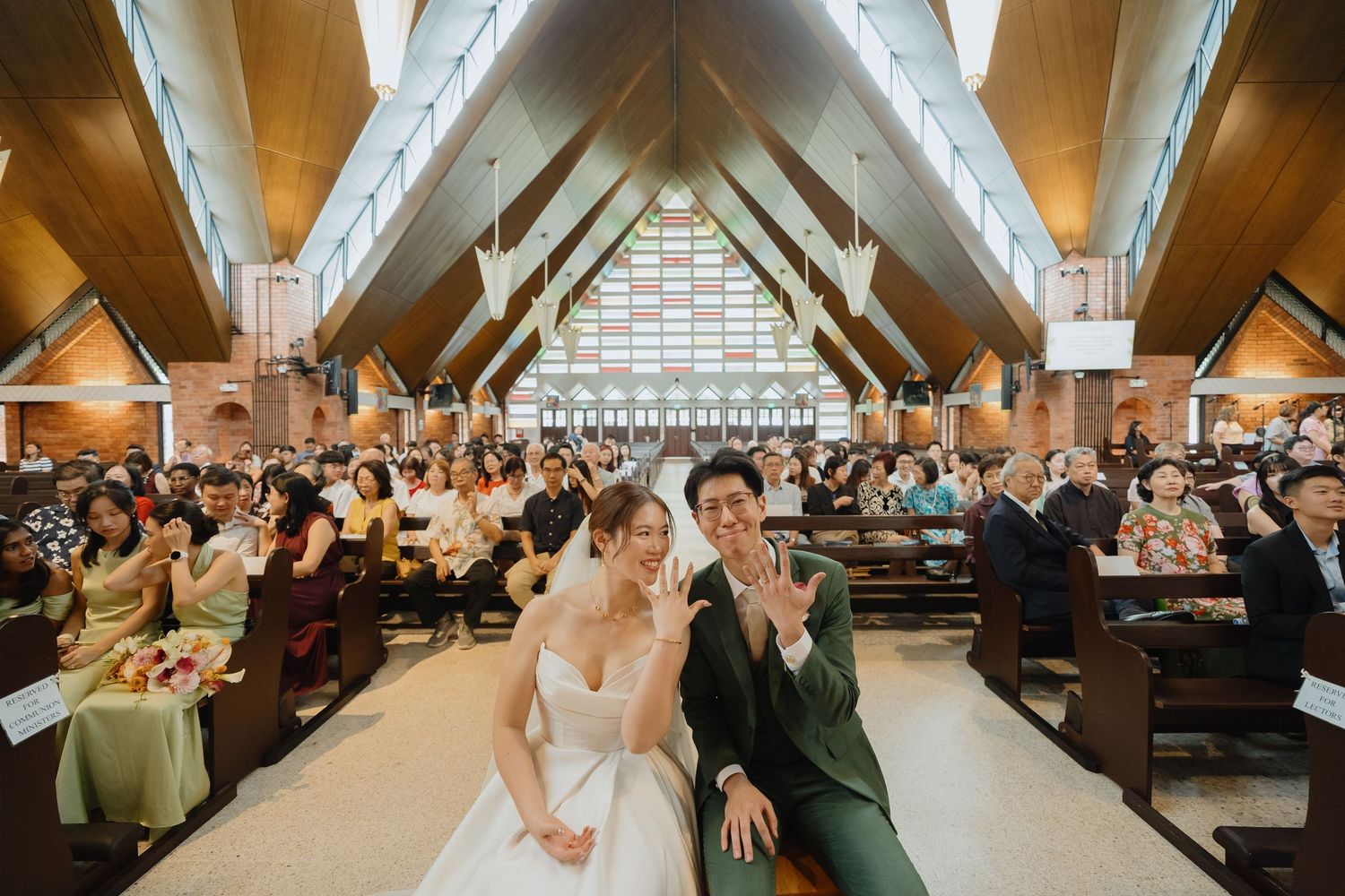Bride and groom smiling at camera during wedding ceremony in elegant church filled with guests.