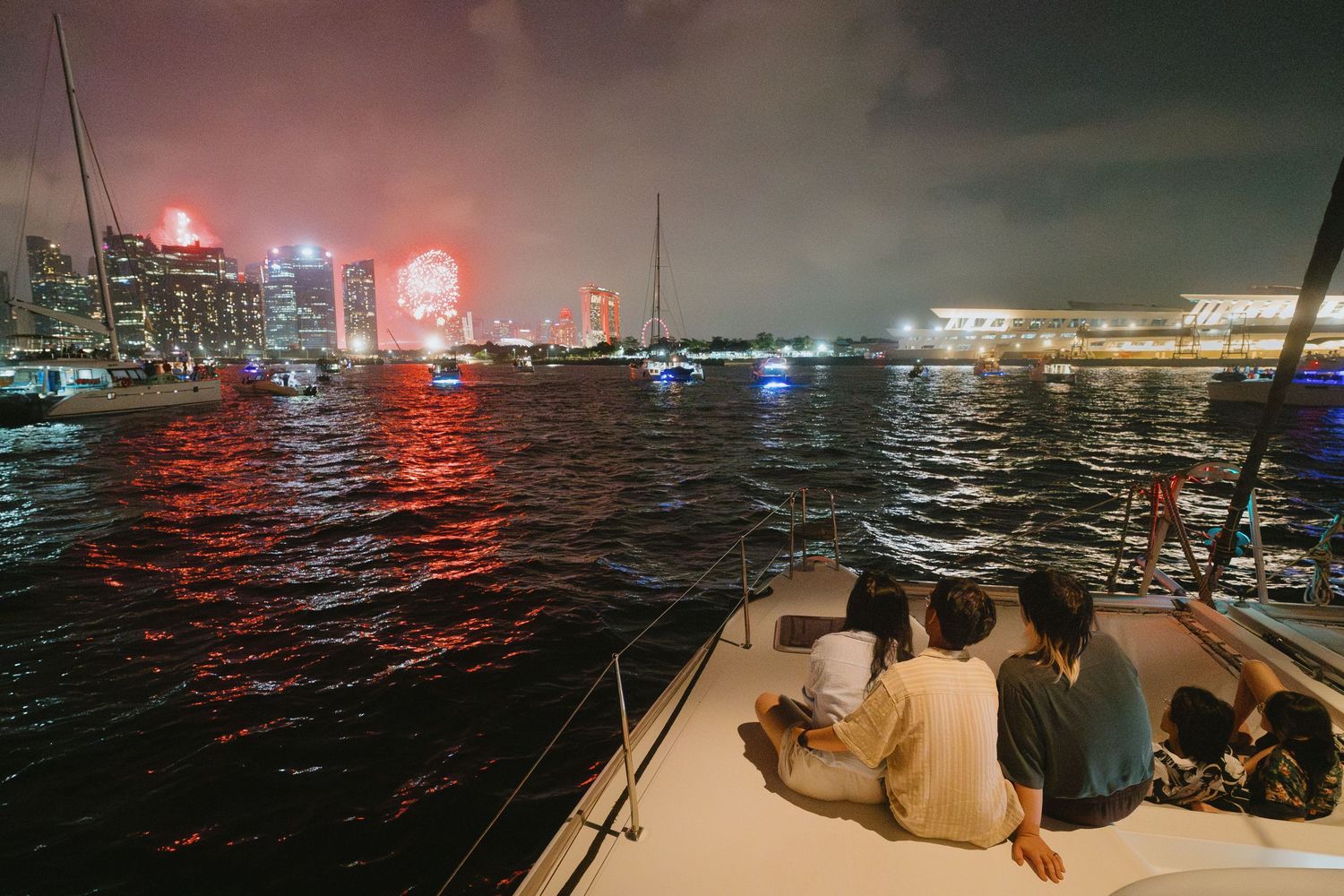 Nighttime view of a harbor with boats reflecting colorful lights on dark water as fog rolls in over the marina.