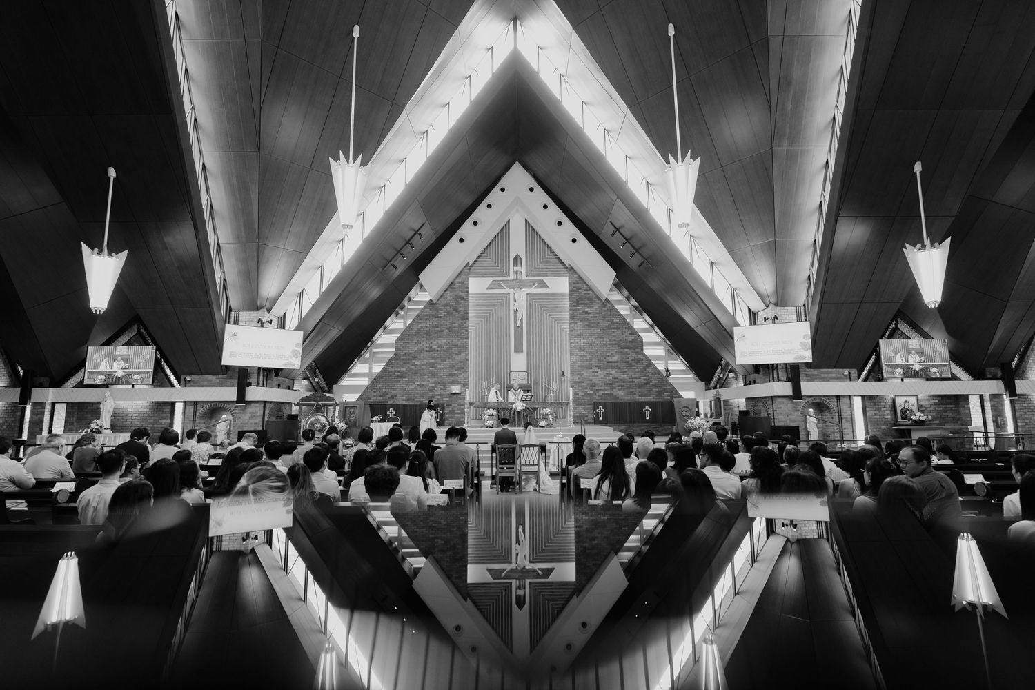 Black and white photo of congregation seated in a modern A-frame church interior with dramatic angular wooden ceiling.