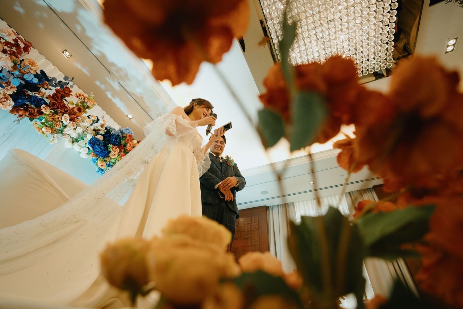 Crystal chandeliers and decorative coral-colored florals create an elegant wedding reception atmosphere.