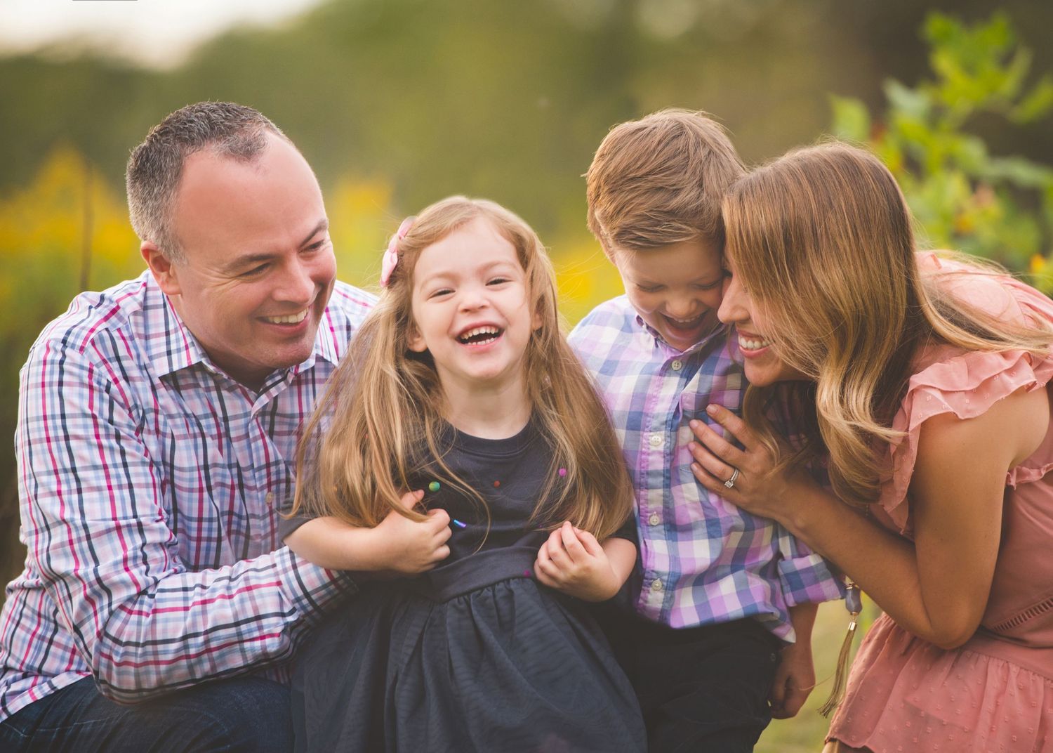 Family of four laughing together beside sunflowers