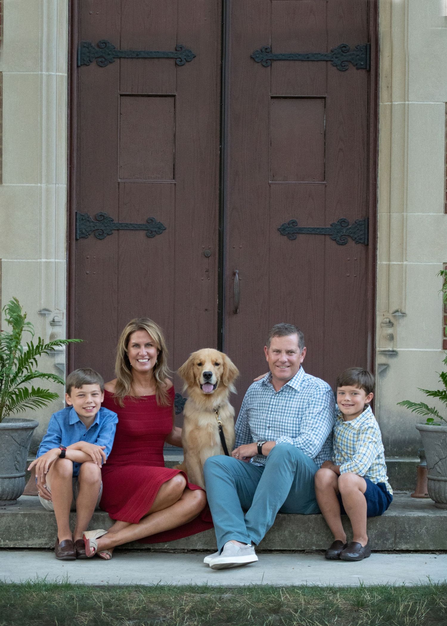 Family of four poses with their dog on church steps before large wooden doors.