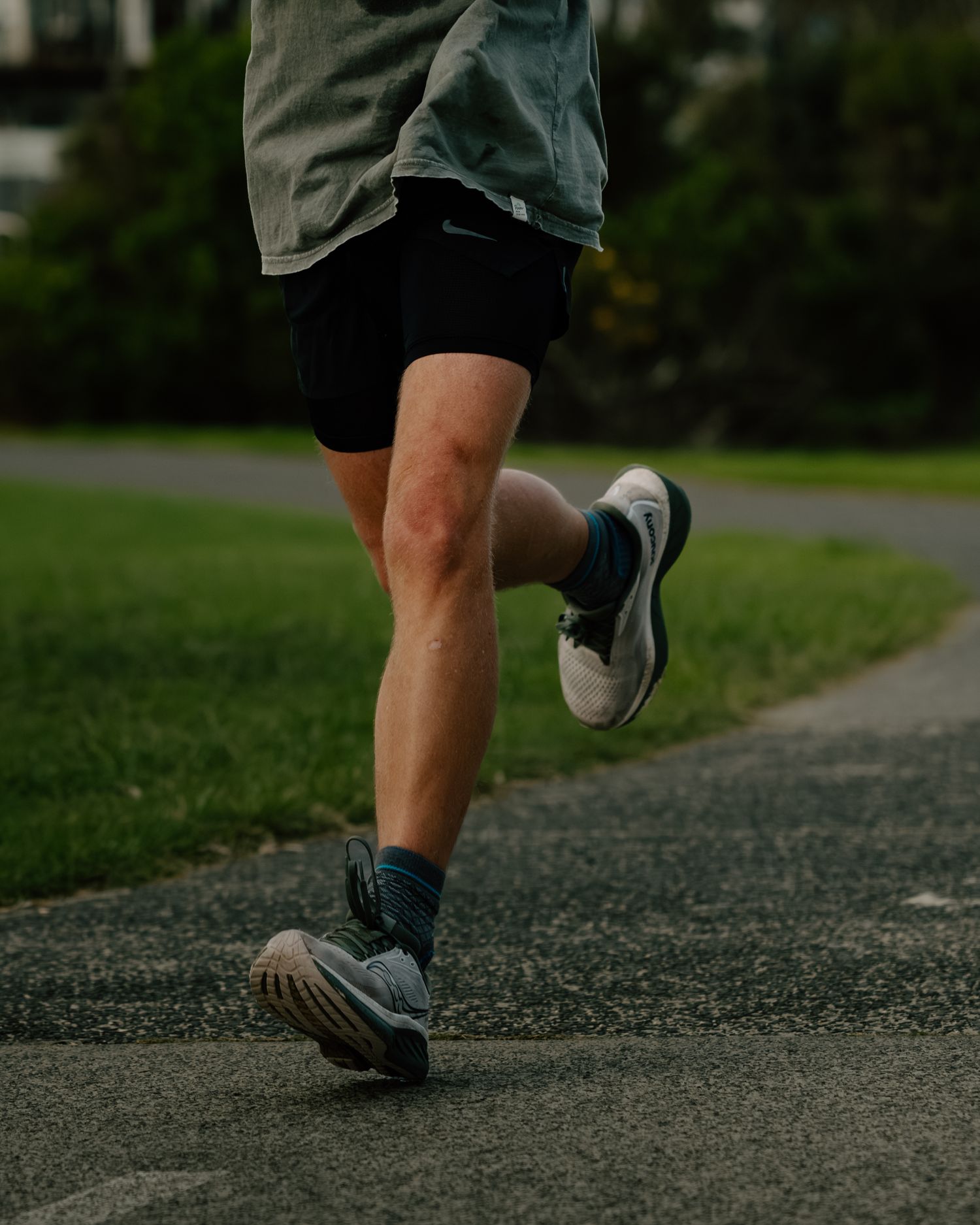 Runner in black shorts and Nike shoes jogging on a park path, captured from the waist down in motion.