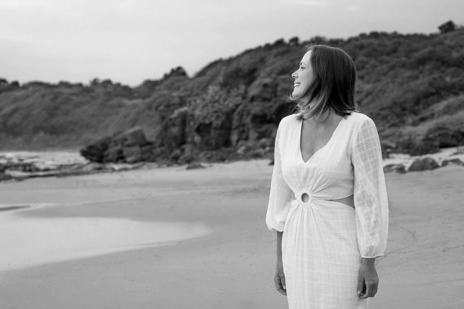 A series of black and white coastal landscape photographs featuring a beach, cliffs, and a figure in white.