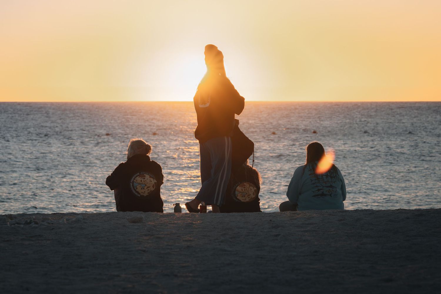 A silhouetted couple sits on rocks by the ocean during a golden sunset creating a romantic atmosphere.