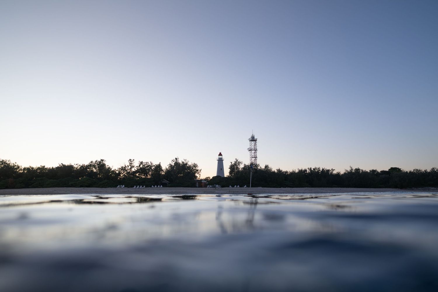 Crisp, minimalist horizon line extends across a serene ocean with a lighthouse in the distance under soft light.