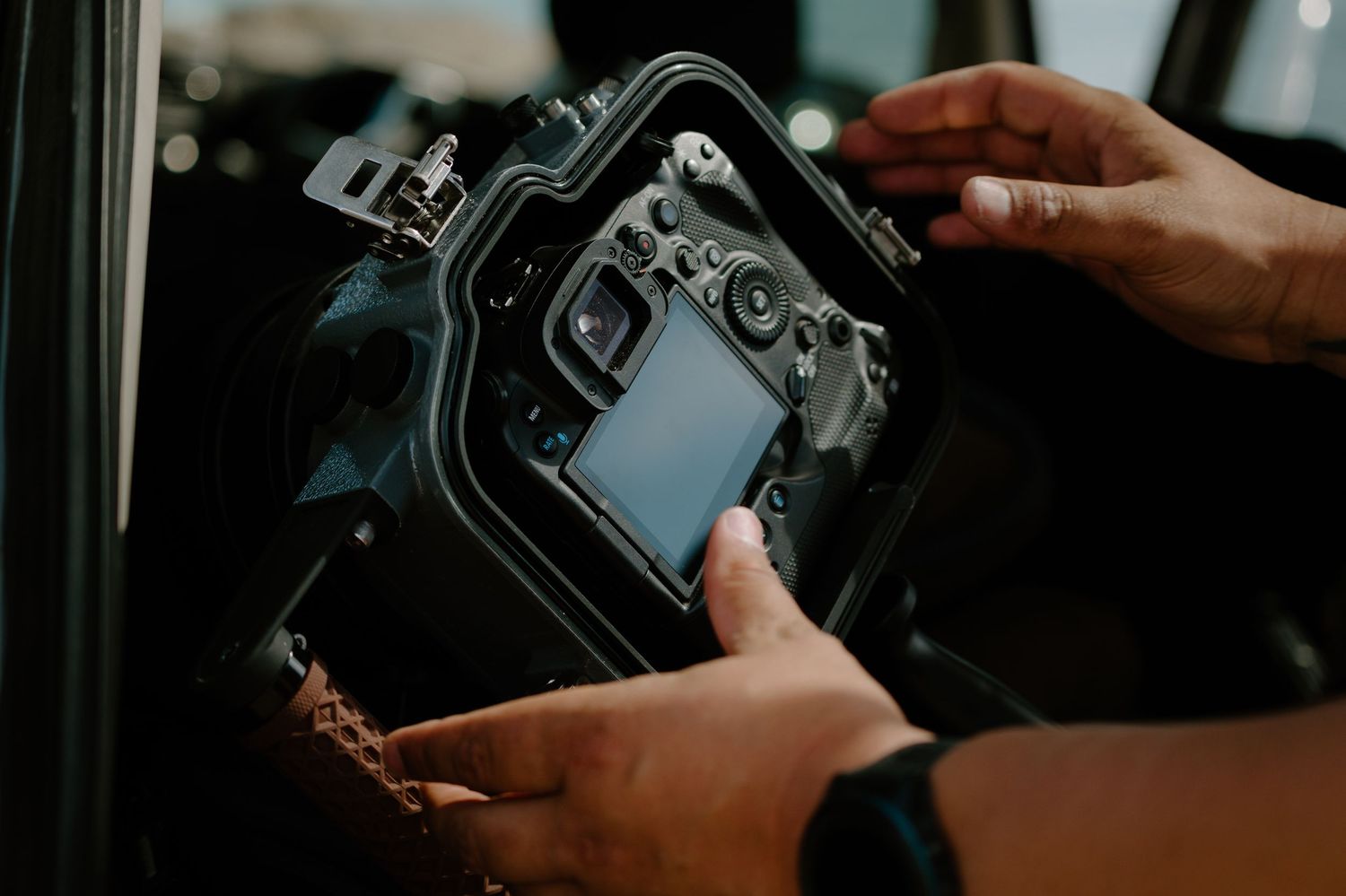 Hands holding a DSLR camera in an underwater housing case, preparing for underwater photography.