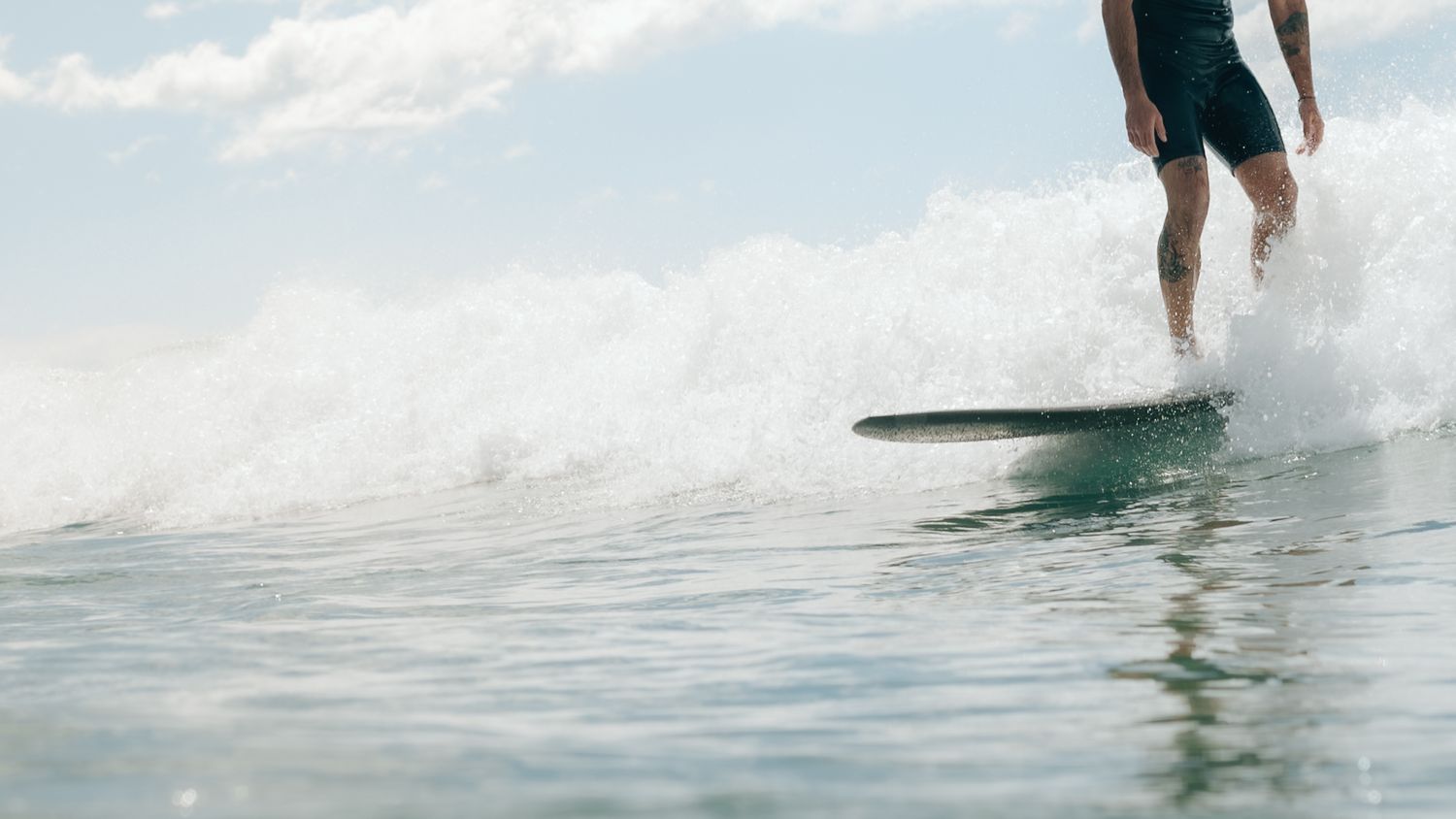 A surfer rides a wave on a longboard in calm ocean waters under a partly cloudy sky.