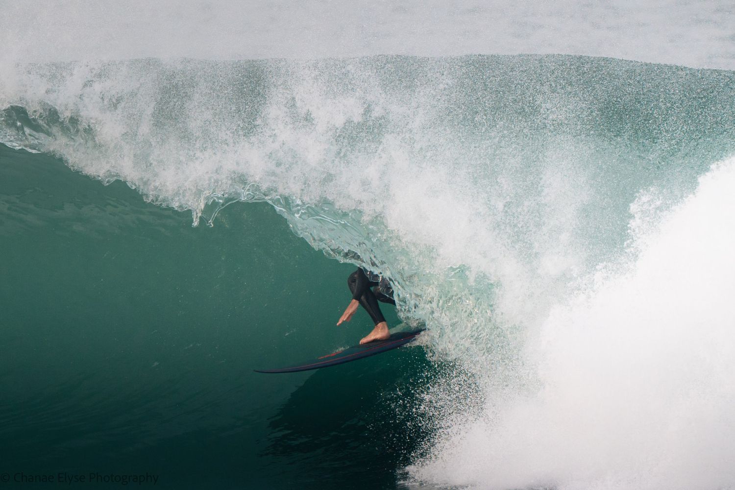 Surfer riding inside a massive barreling wave on a surfboard in clear turquoise ocean water.