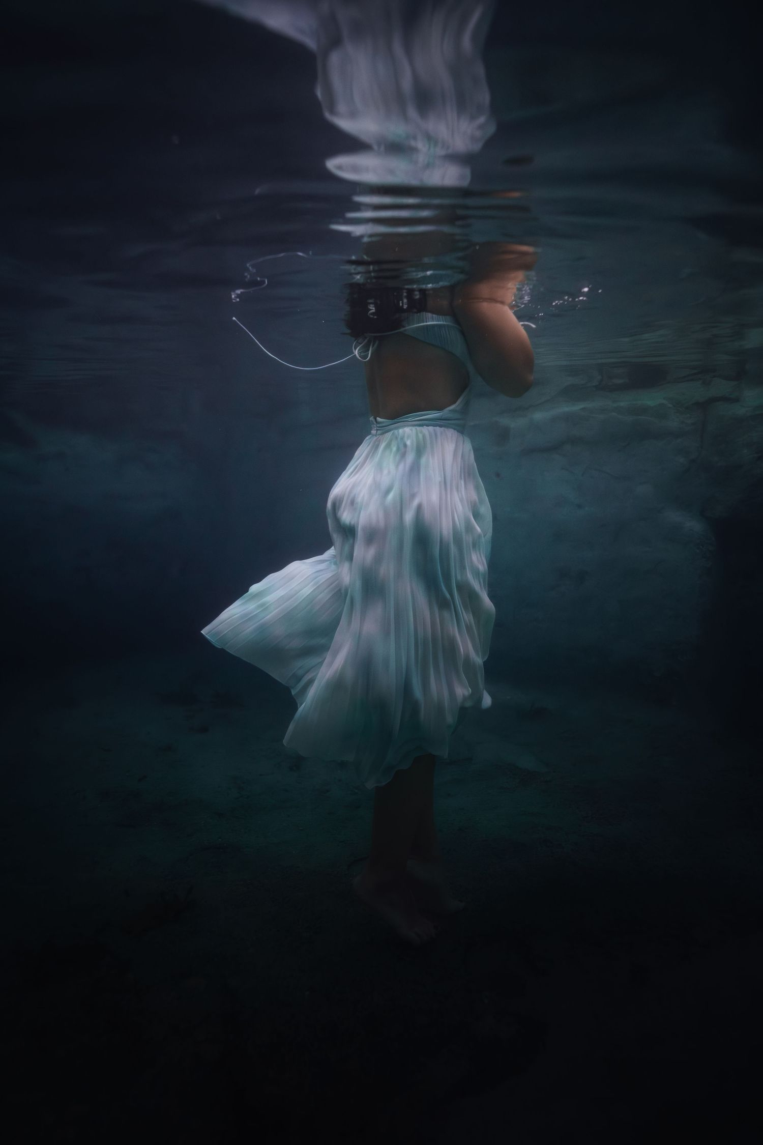 Ethereal underwater photo series showing flowing white dress fabric in dark moody blue water creating dreamy movement.