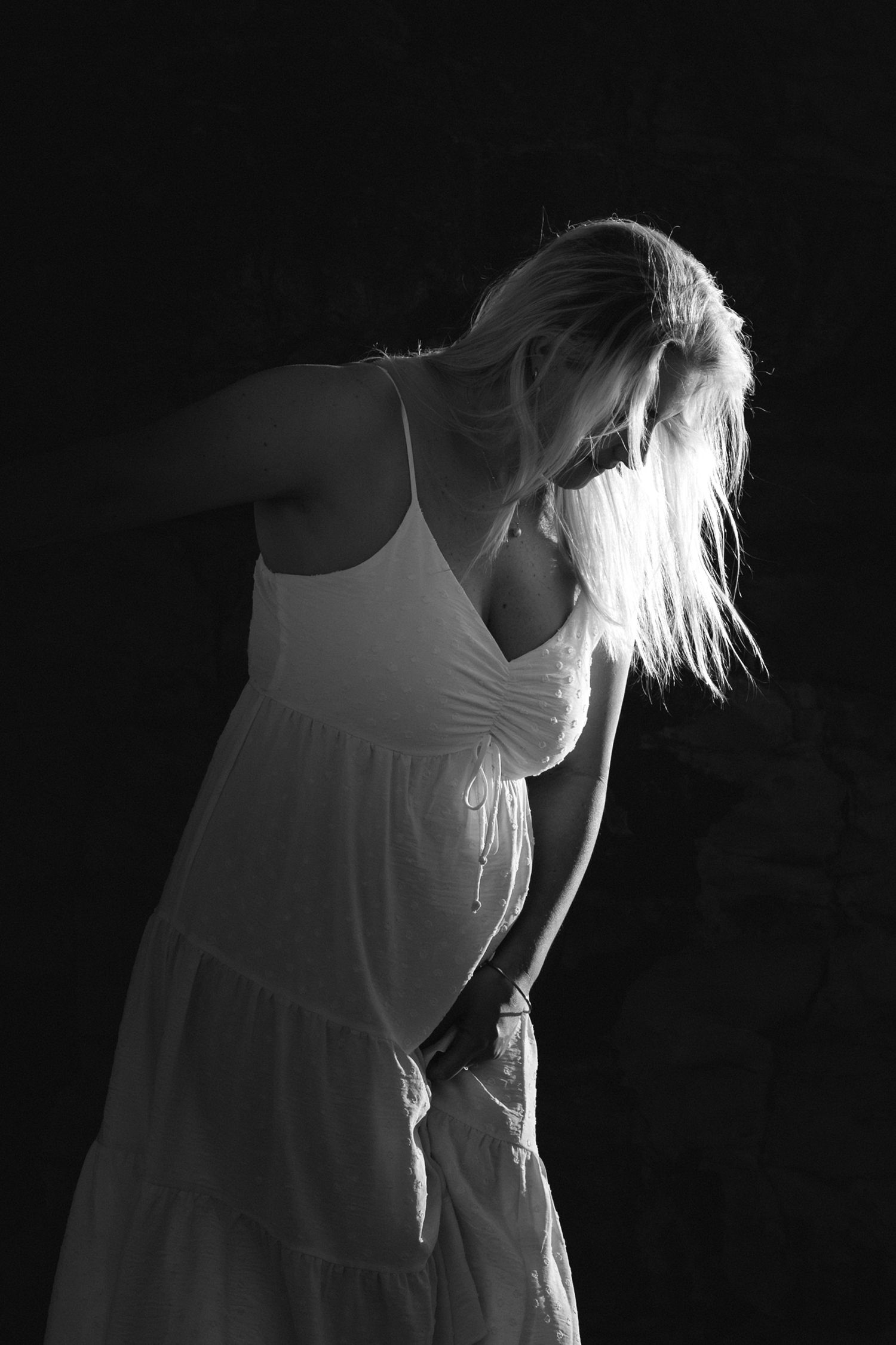 A dramatic black and white portrait of a person in a white dress with flowing hair against a dark background.