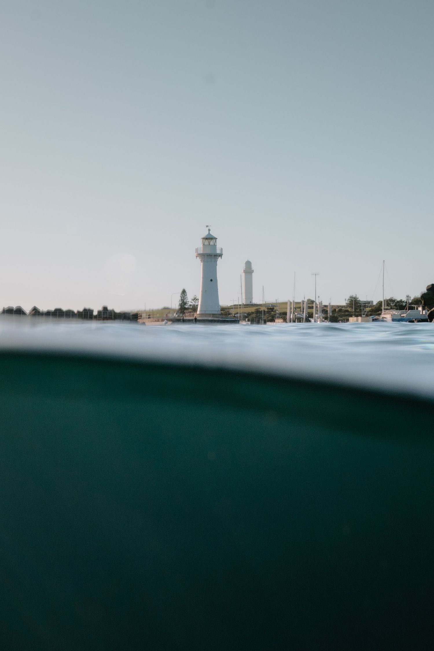 A minimalist seascape showing a white lighthouse on the horizon against a misty blue sky and dark ocean waters.