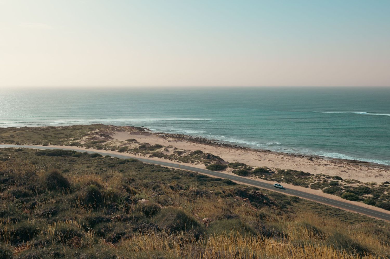 Panoramic coastal view showing rolling sand dunes and turquoise ocean waters stretching along the shoreline on a sunny day.