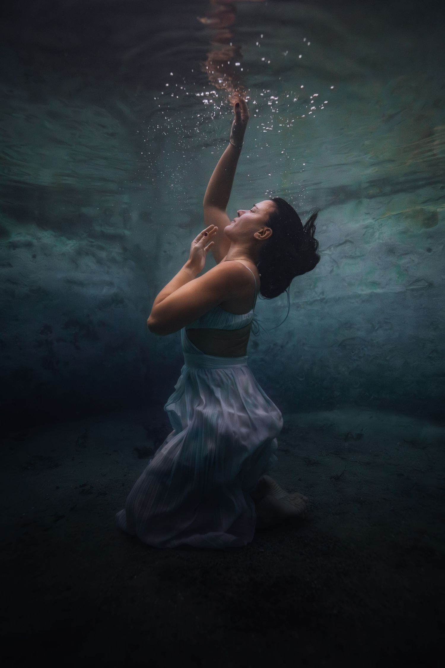 Underwater dancer in flowing purple dress creates ethereal movement sequence in dark aquatic setting.