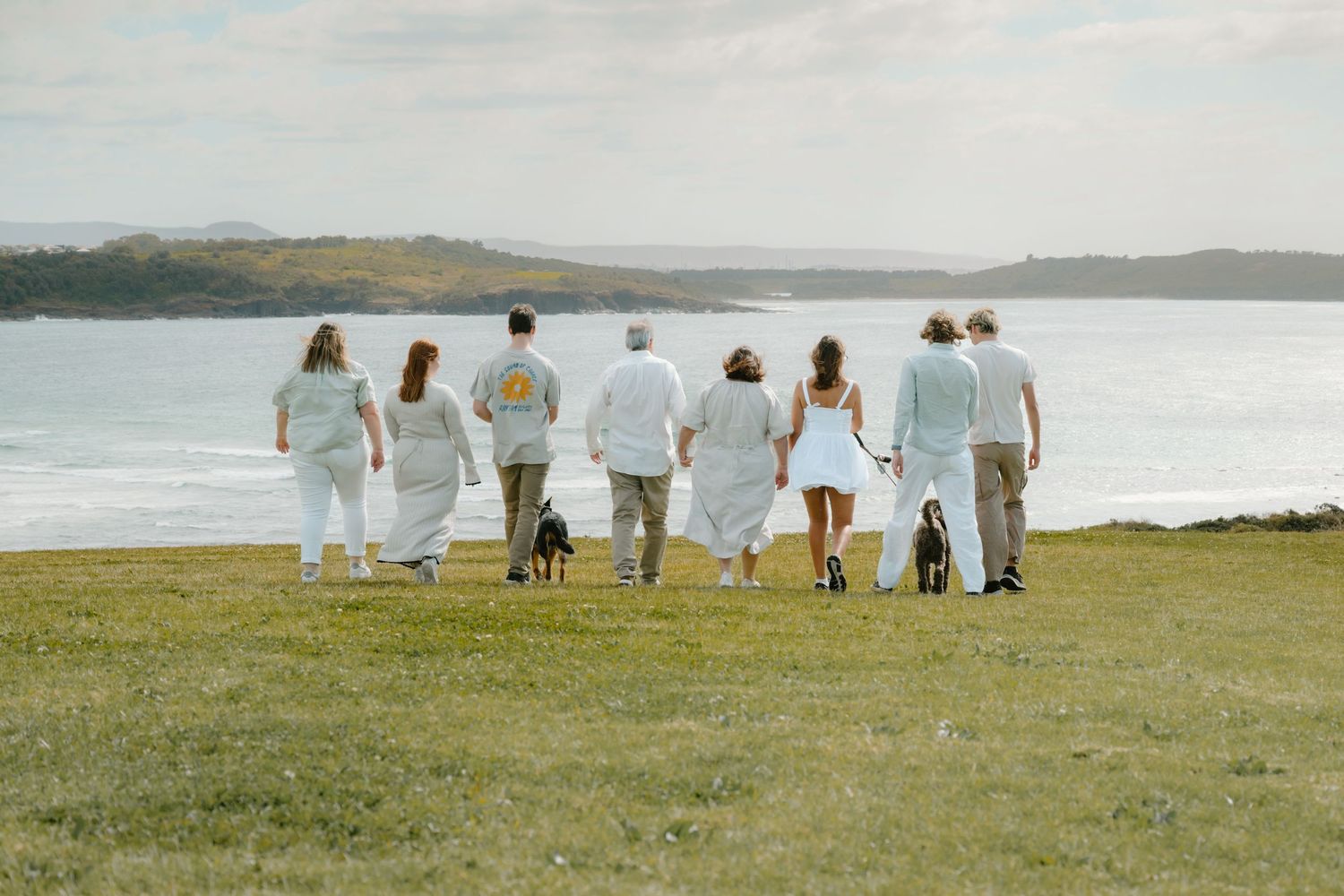 Group in white attire walks along scenic coastal cliffs with ocean views and green grassland.