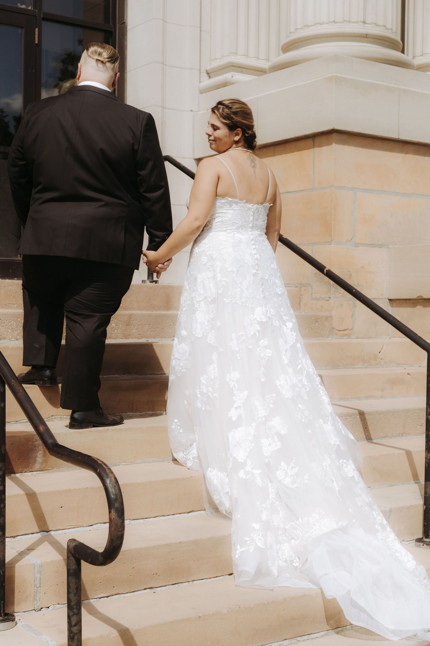 Sequence showing couple ascending stone steps of a building with ornate columns.