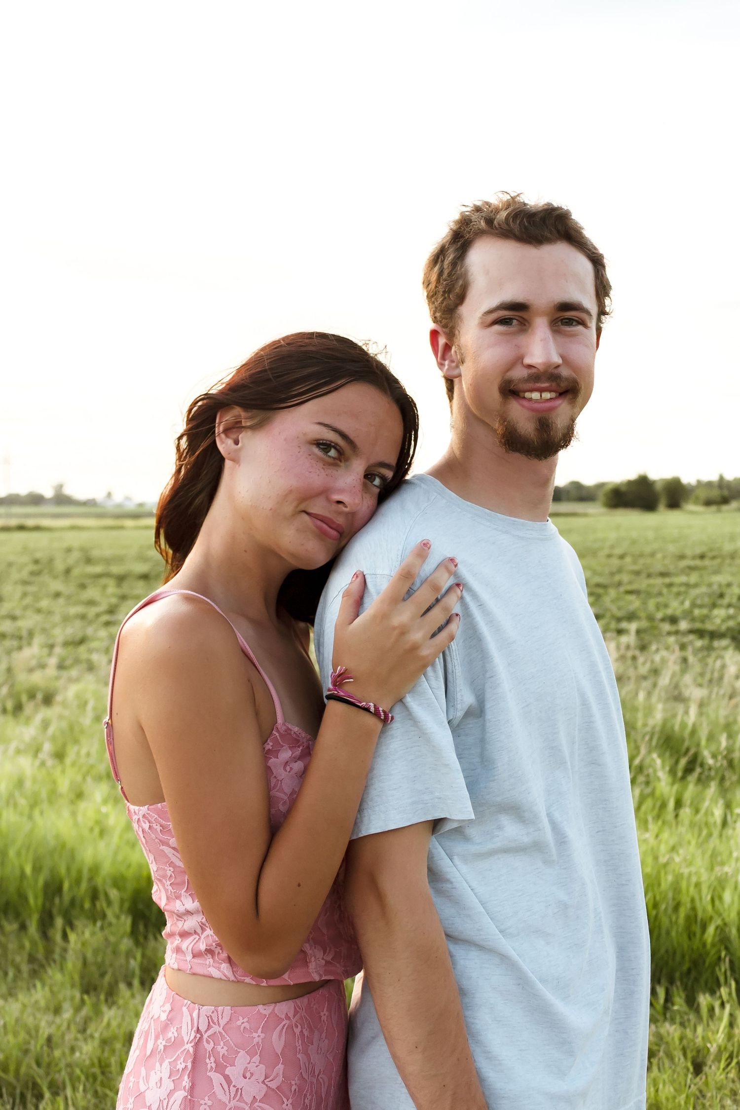 Couple poses playfully in green summer field during photoshoot.
