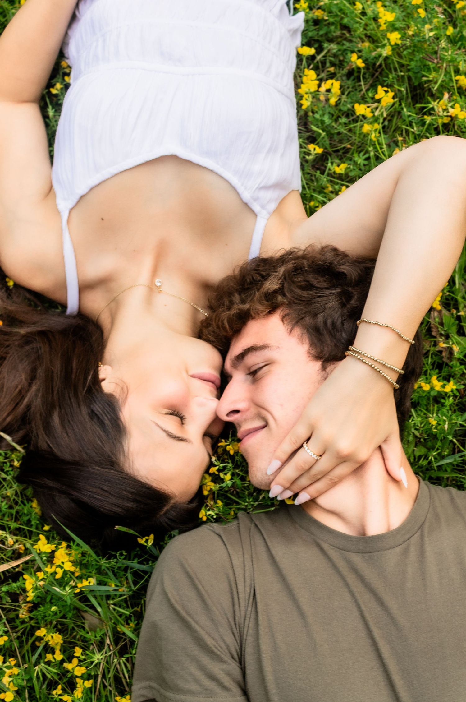 A couple lies in a field of yellow flowers sharing an intimate moment.