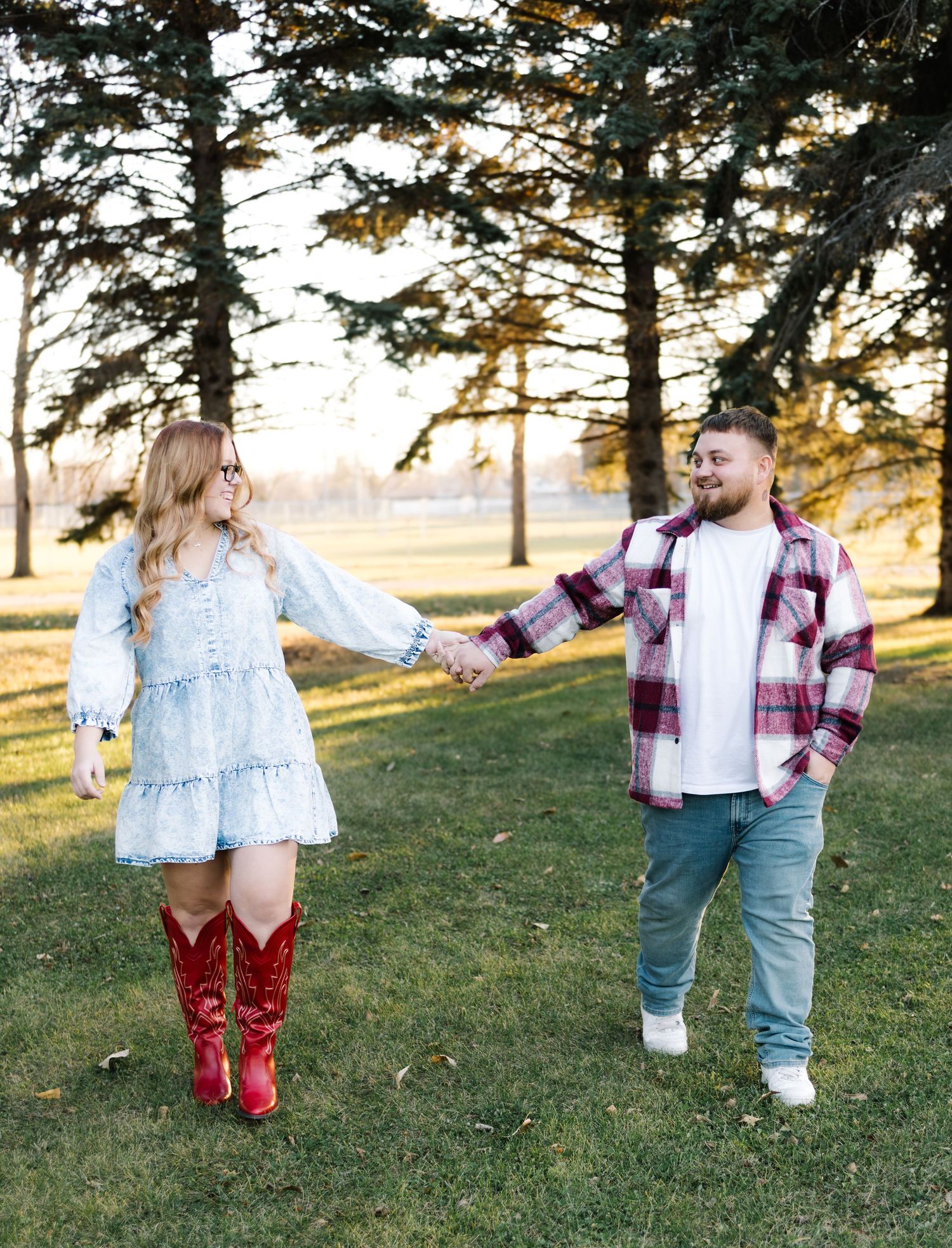 Couple holding hands in a park, woman in red cowboy boots and blue dress, man in plaid shirt and jeans.
