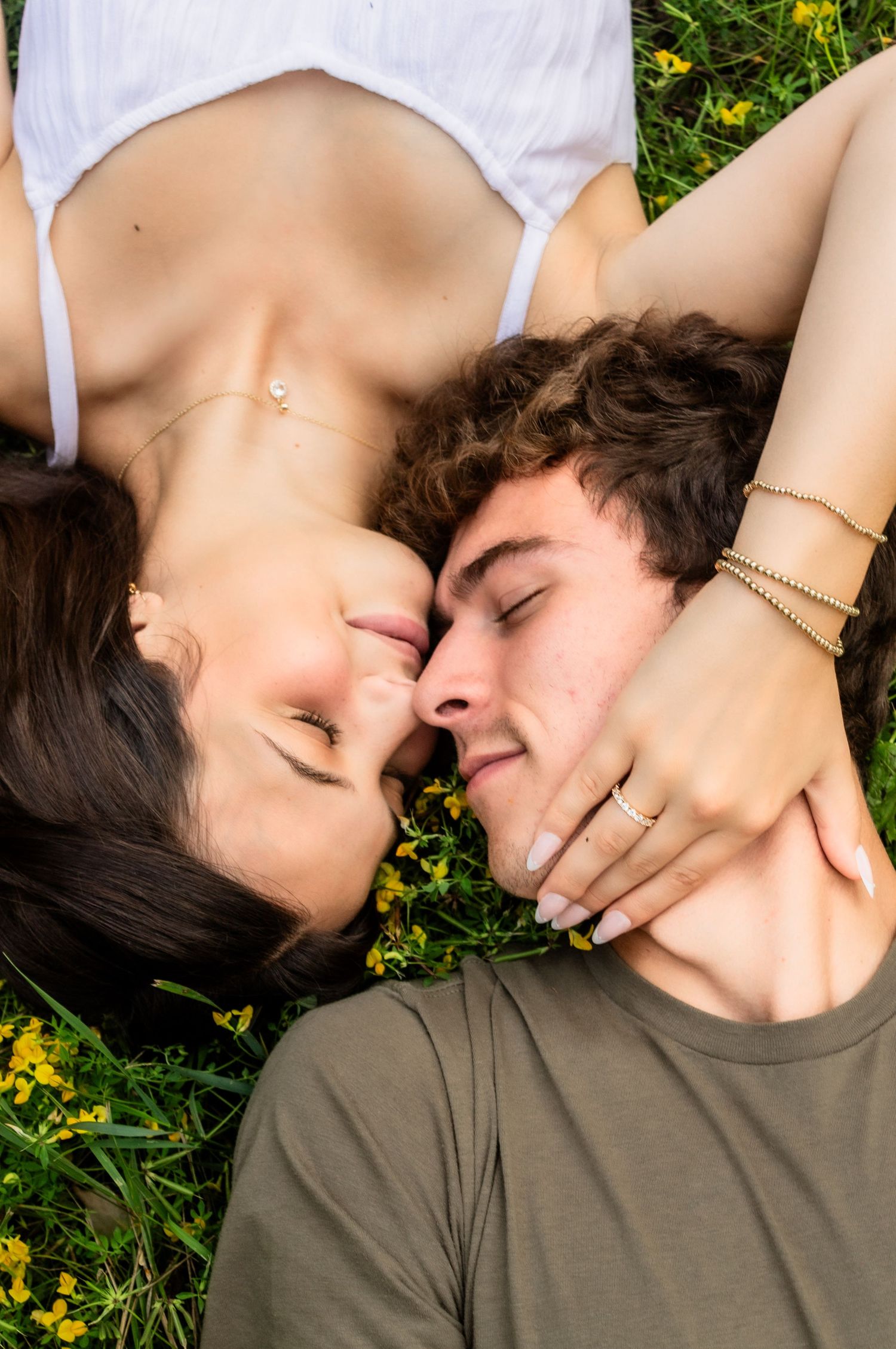 Couple lying in grass surrounded by yellow flowers sharing an intimate moment together.