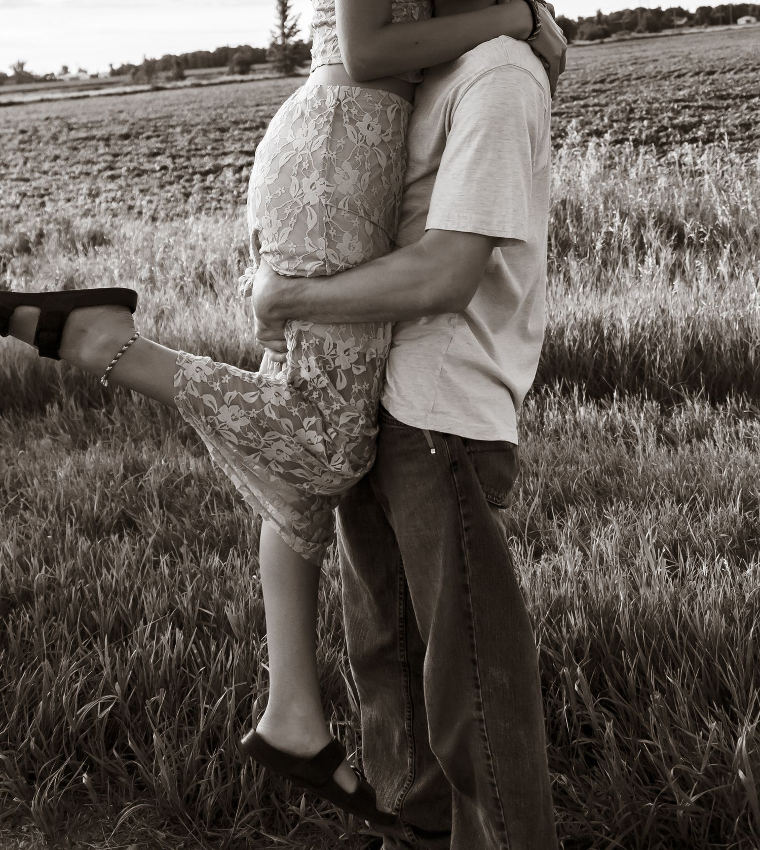 A couple embraces while standing in a grassy field, captured in black and white.