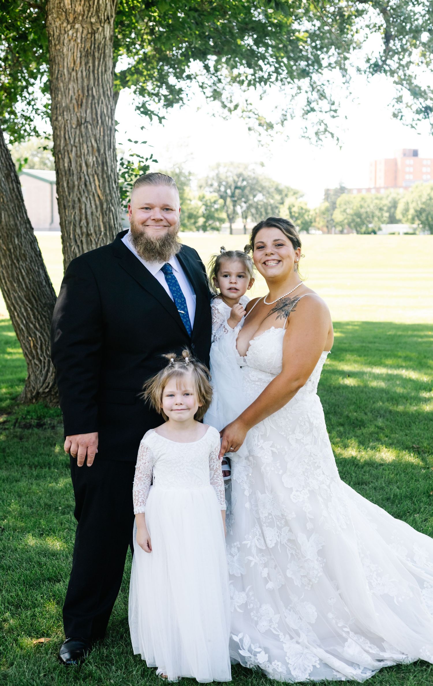 Wedding party members gather around bride in flowing white dress for outdoor portraits.