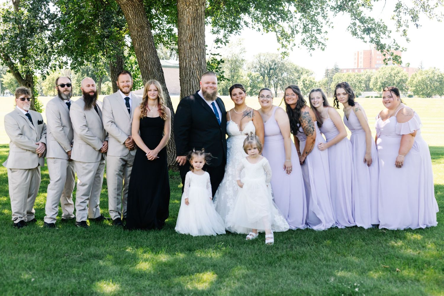Wedding party group photo with bridesmaids in lavender dresses standing together on a lawn.