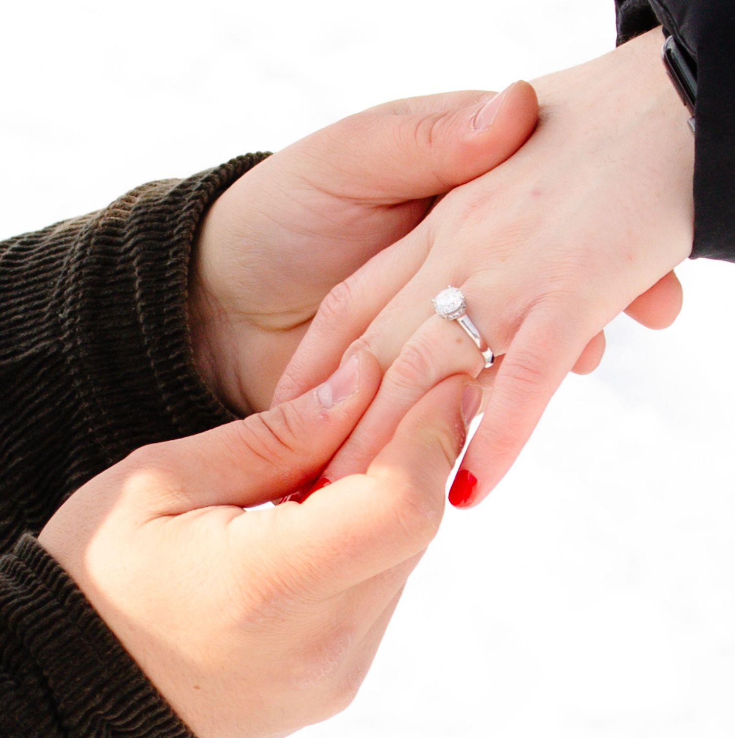 Hands displaying an engagement ring with red nail polish.