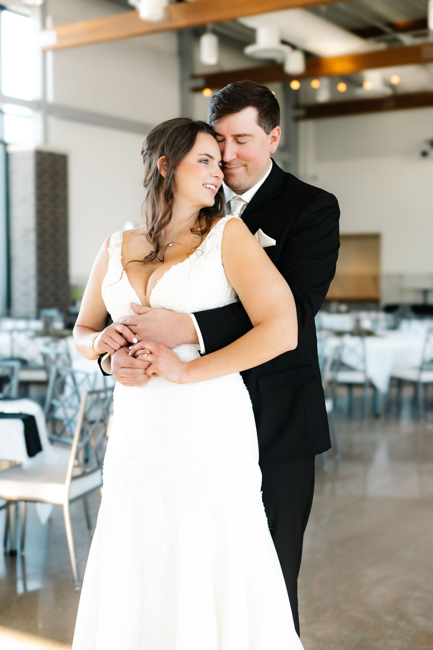 Bride and groom share first dance in elegant wedding venue, bride in white lace gown, groom in black tuxedo.
