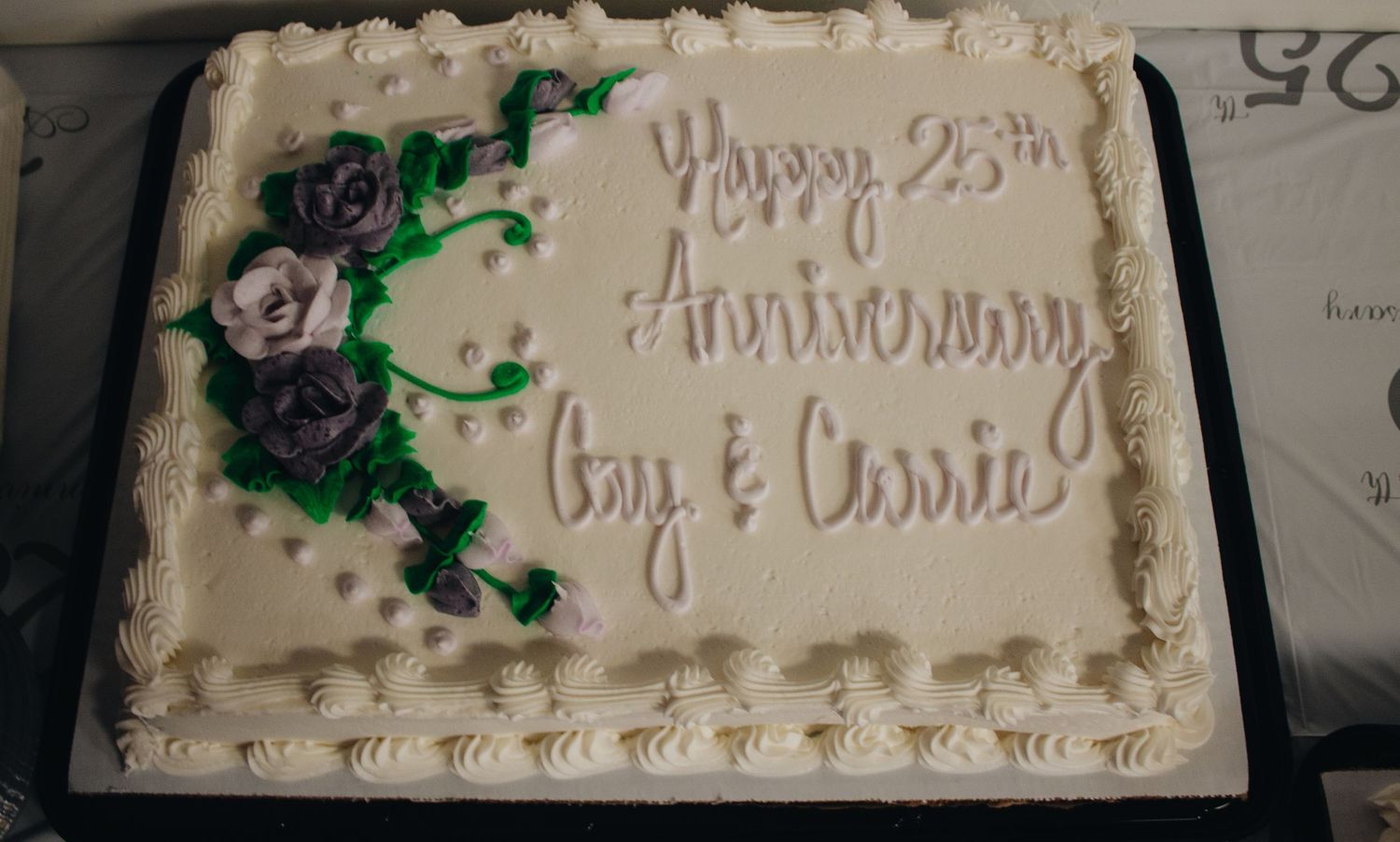 White frosted sheet cake with purple floral decorations and anniversary text.