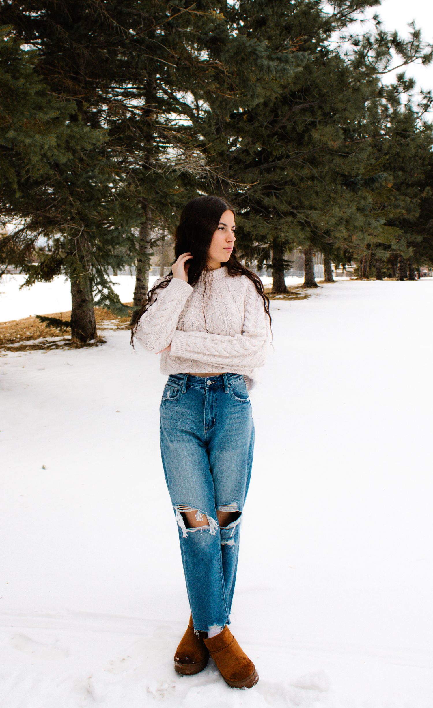 Stylish winter fashion look with cozy sweater and distressed denim in snow covered landscape.