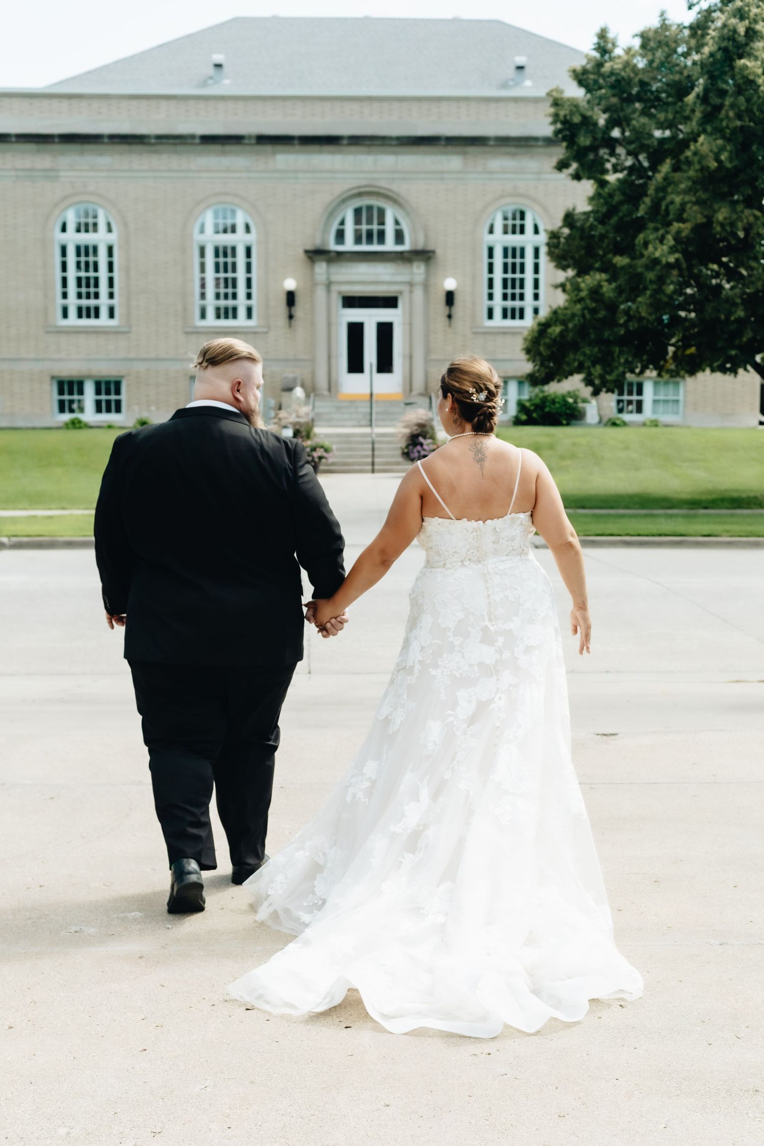 Wedding couple walking together across a courtyard with classic architecture in background.