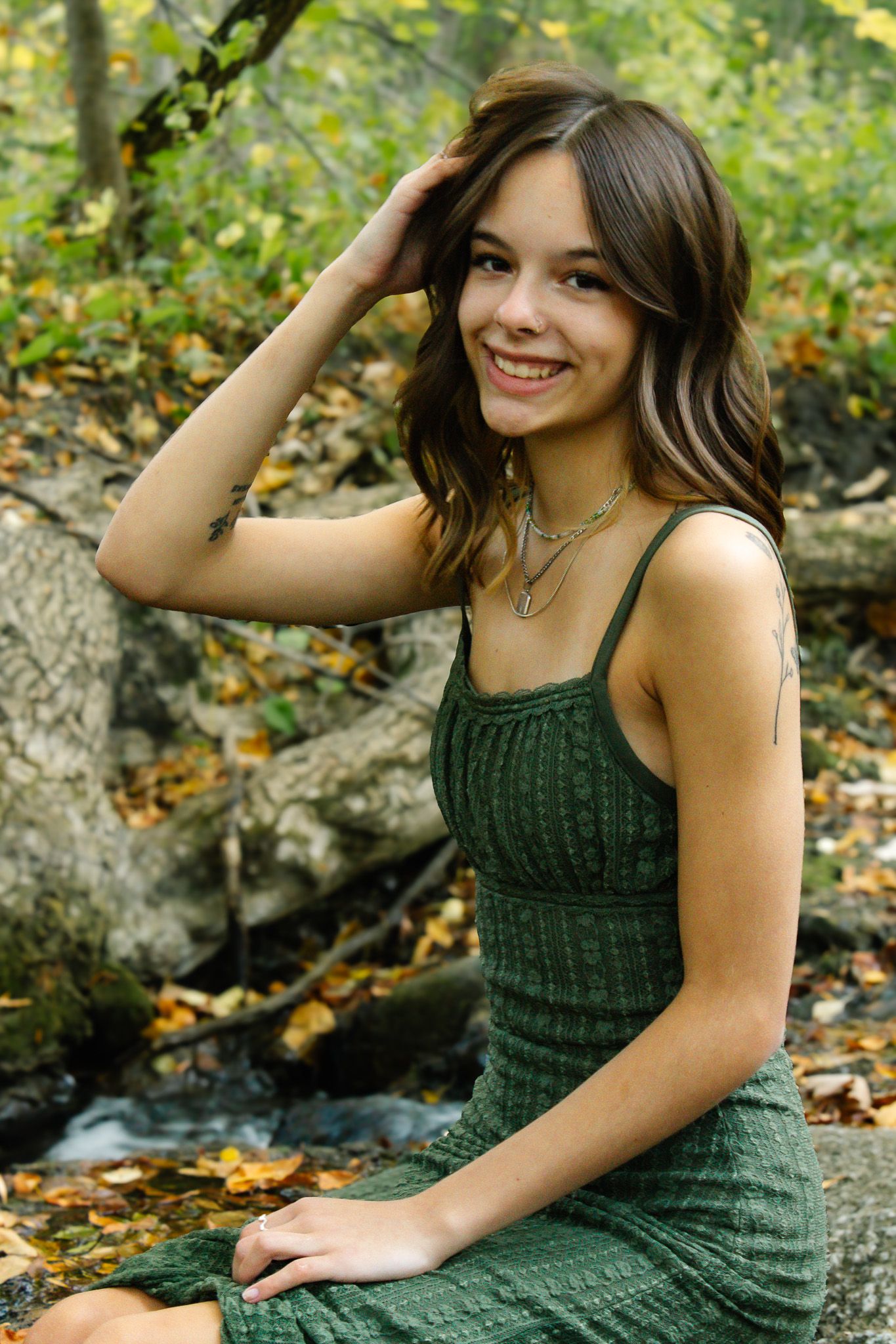 Forest portrait session featuring dark green knit dress by stream in autumn setting.