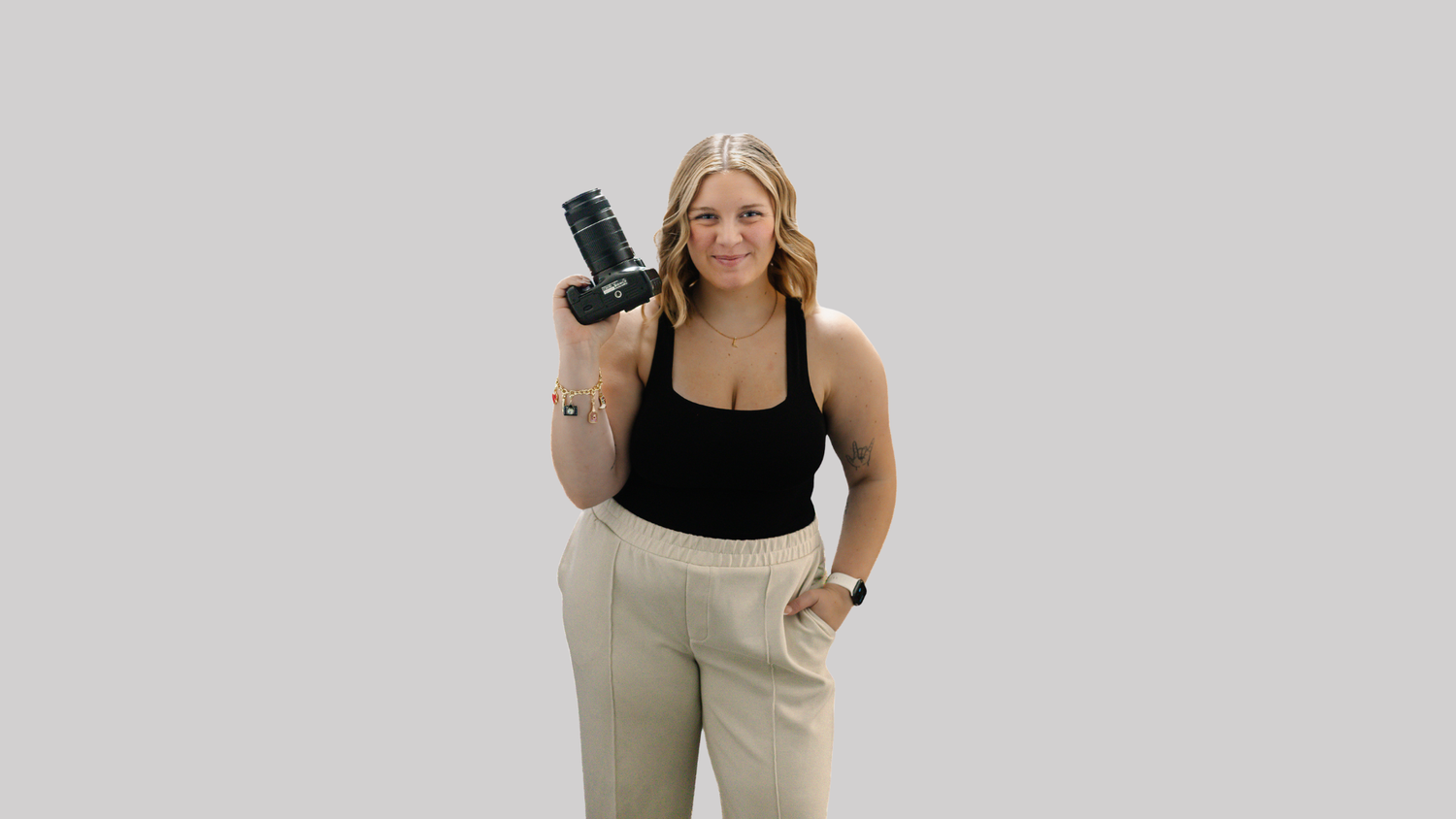 Photographer in casual attire holds professional camera while standing against light background.