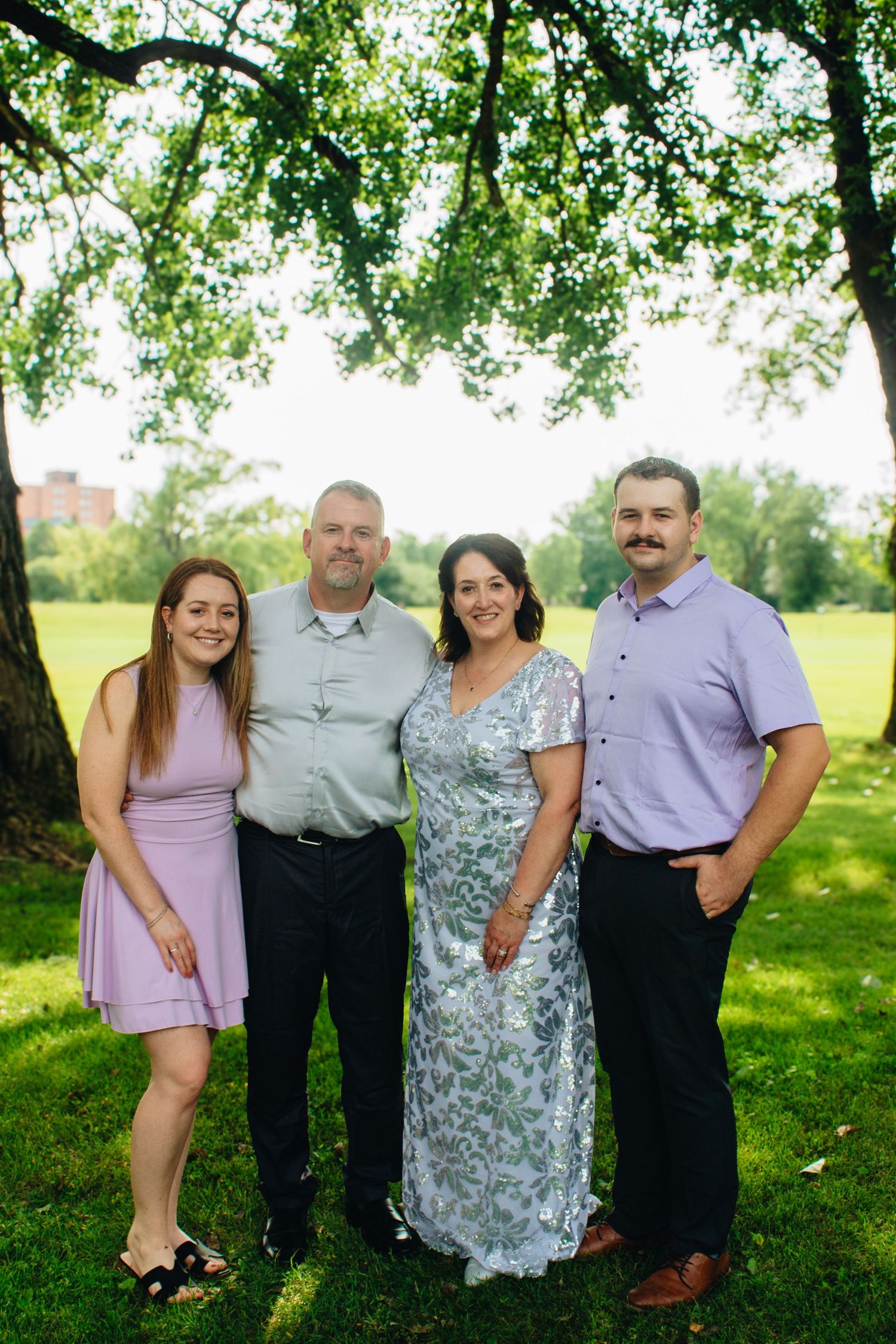 Family group poses together for portraits under shady trees on a sunny summer day.