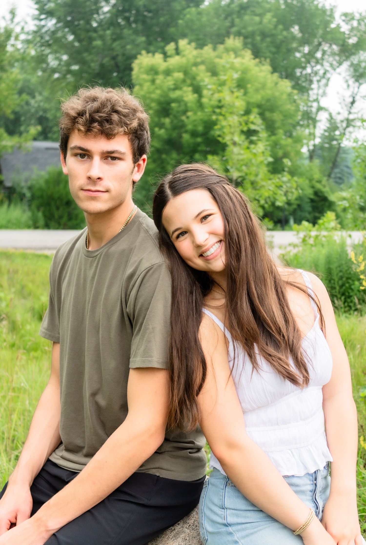 A couple sits together and poses playfully in a natural outdoor setting with green foliage.